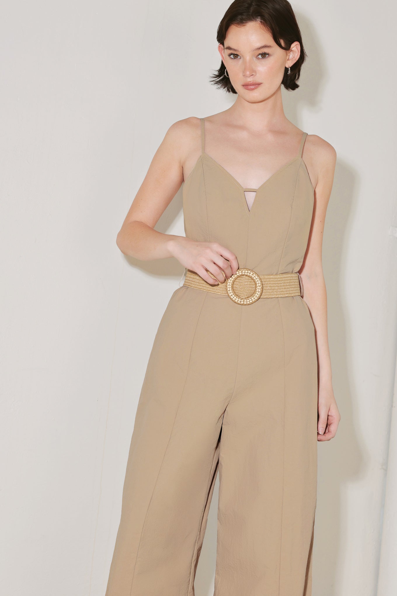 Woman wearing a beige jumpsuit featuring cami top, straps, contrasting belt, wide leg and back zipper closure | FREEMARKET | Flying Tomato