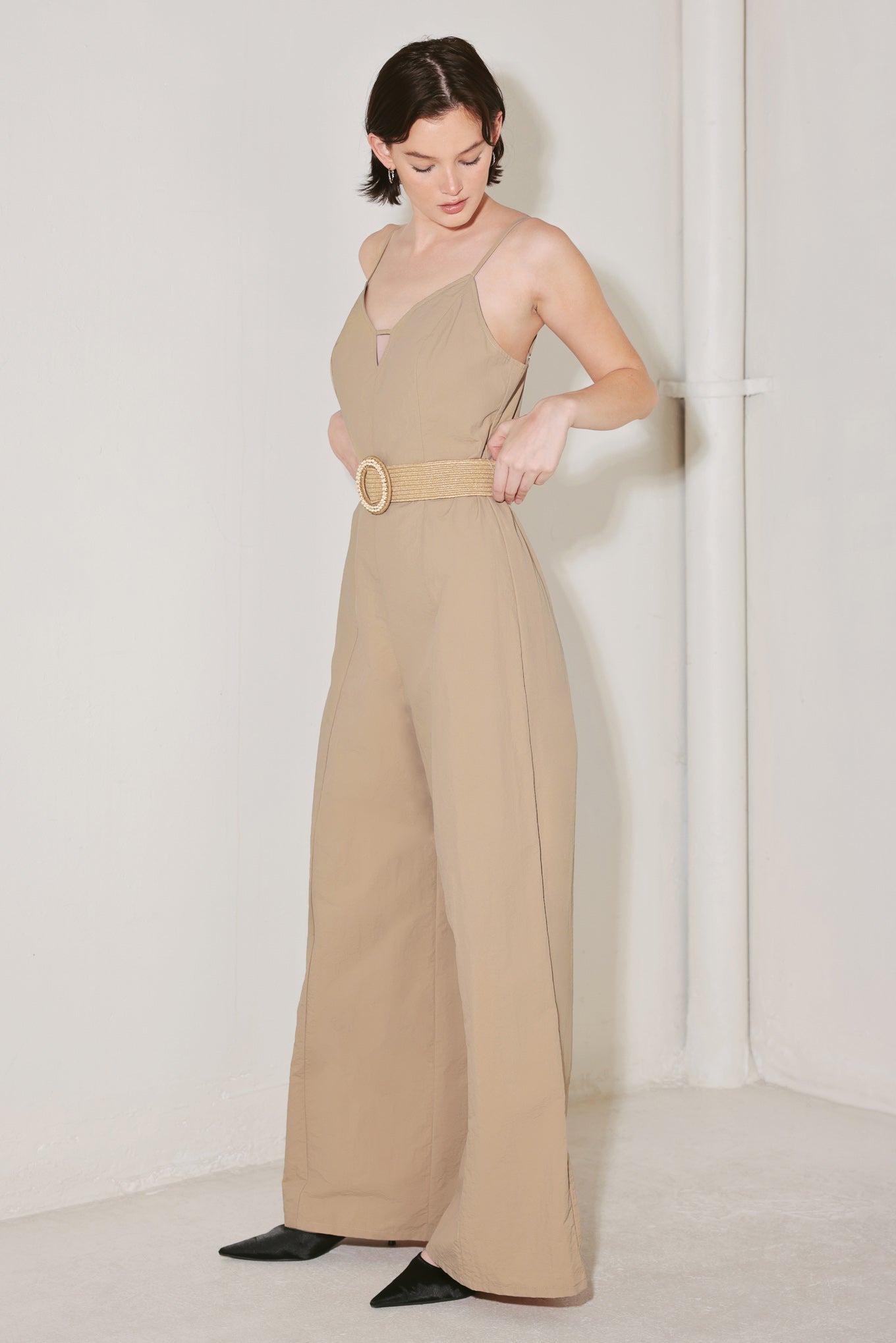 Woman wearing a beige jumpsuit featuring cami top, straps, contrasting belt, wide leg and back zipper closure | FREEMARKET | Flying Tomato