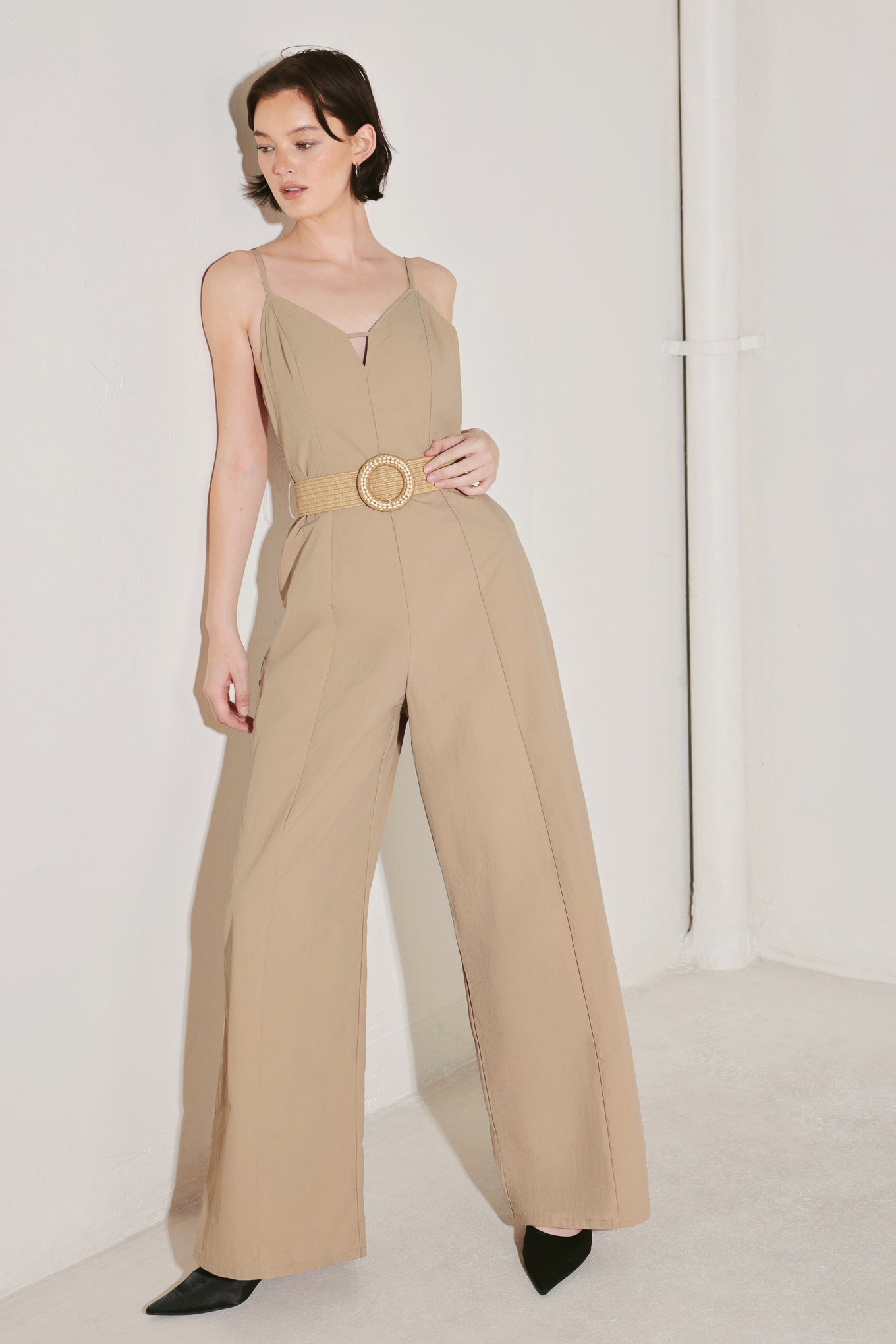 Woman wearing a beige jumpsuit featuring cami top, straps, contrasting belt, wide leg and back zipper closure | FREEMARKET | Flying Tomato