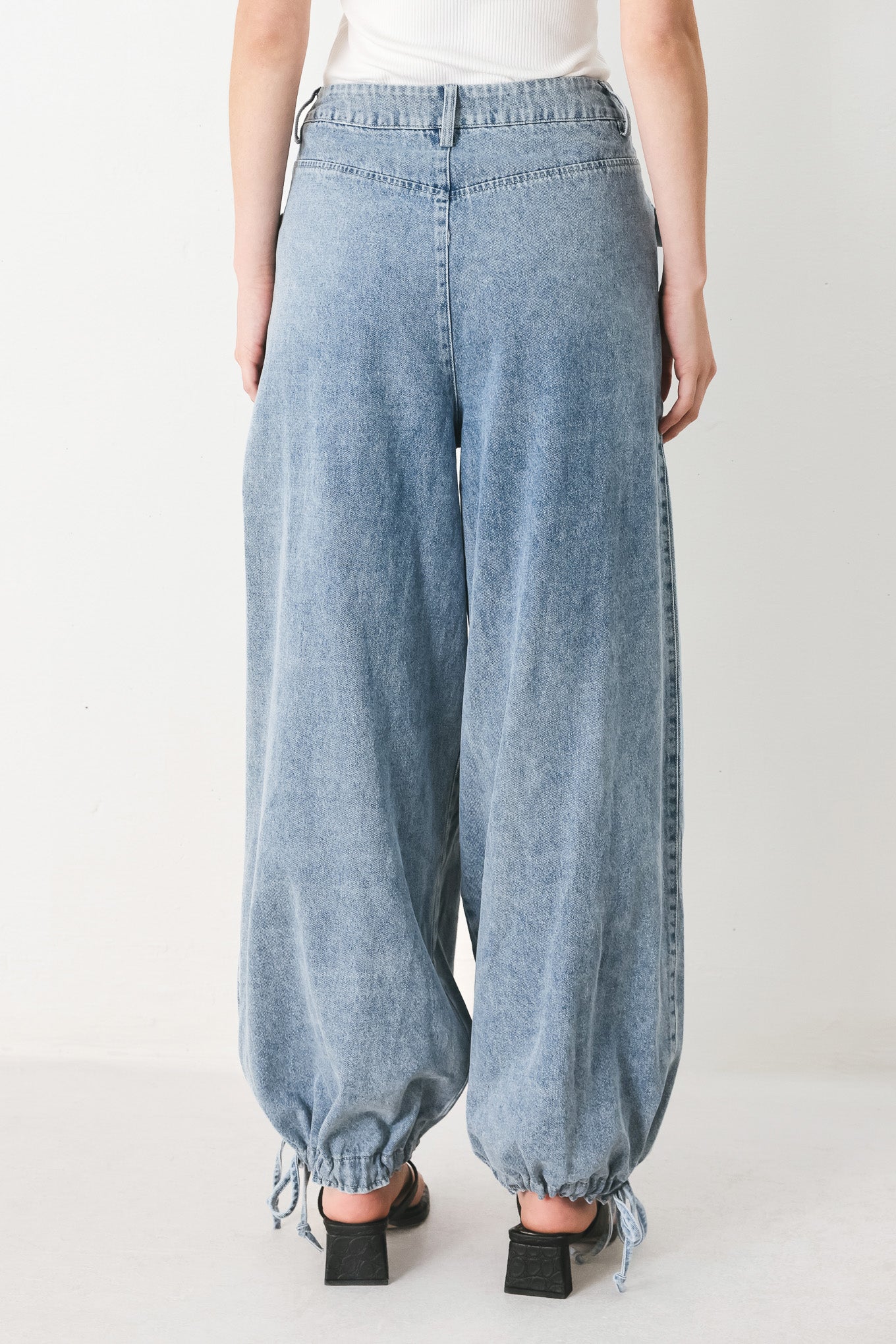 Woman wearing washed denim pants featuring front closure, front pockets, balloon leg with bottom tie | FREEMARKET