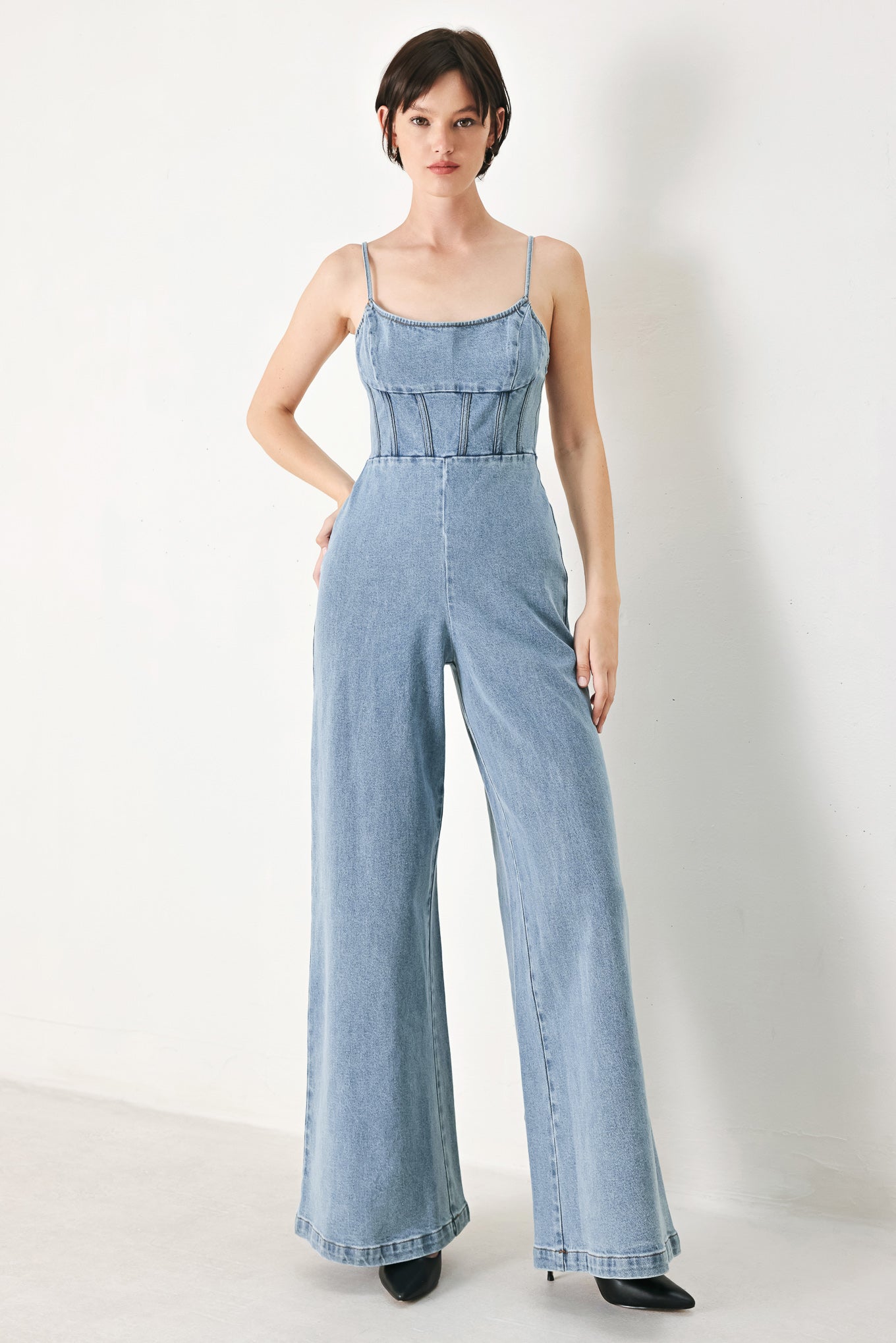 A washed denim jumpsuit featuring U neckline, straps, waist yoke, wide leg, bare back with zipper closure