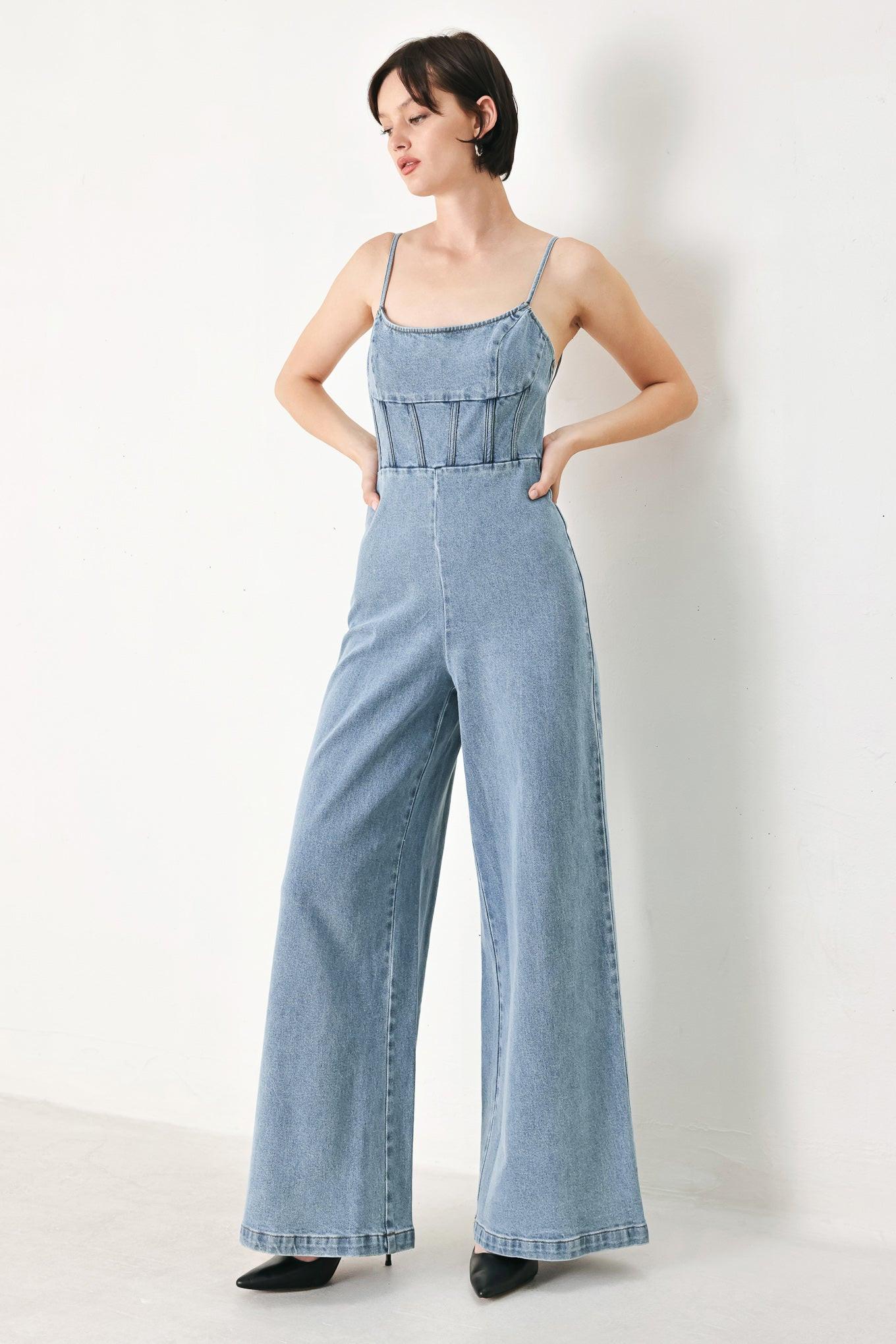 A washed denim jumpsuit featuring U neckline, straps, waist yoke, wide leg, bare back with zipper closure