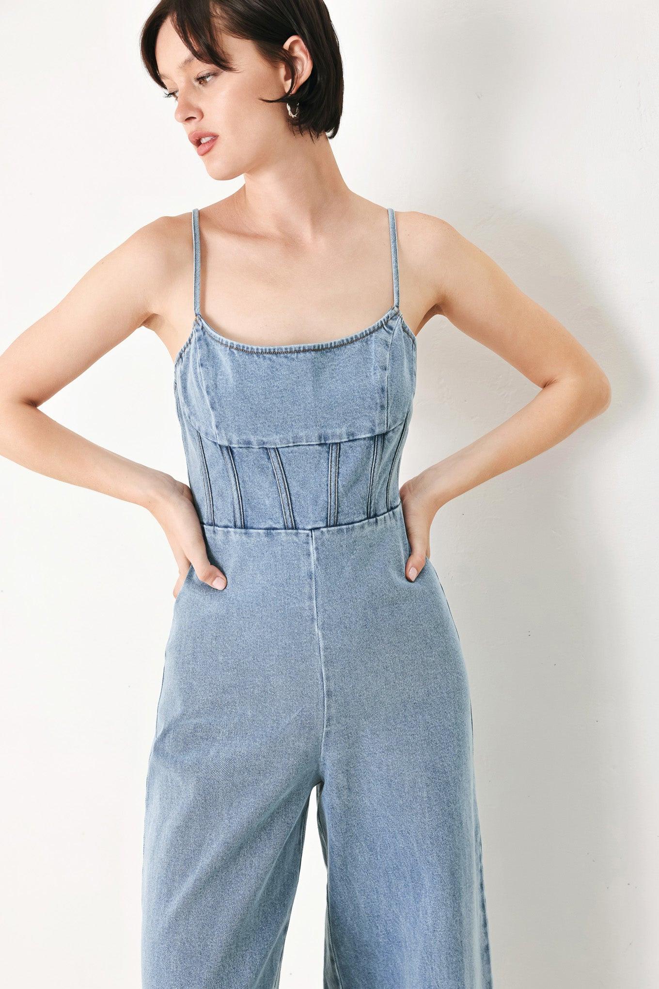 A washed denim jumpsuit featuring U neckline, straps, waist yoke, wide leg, bare back with zipper closure