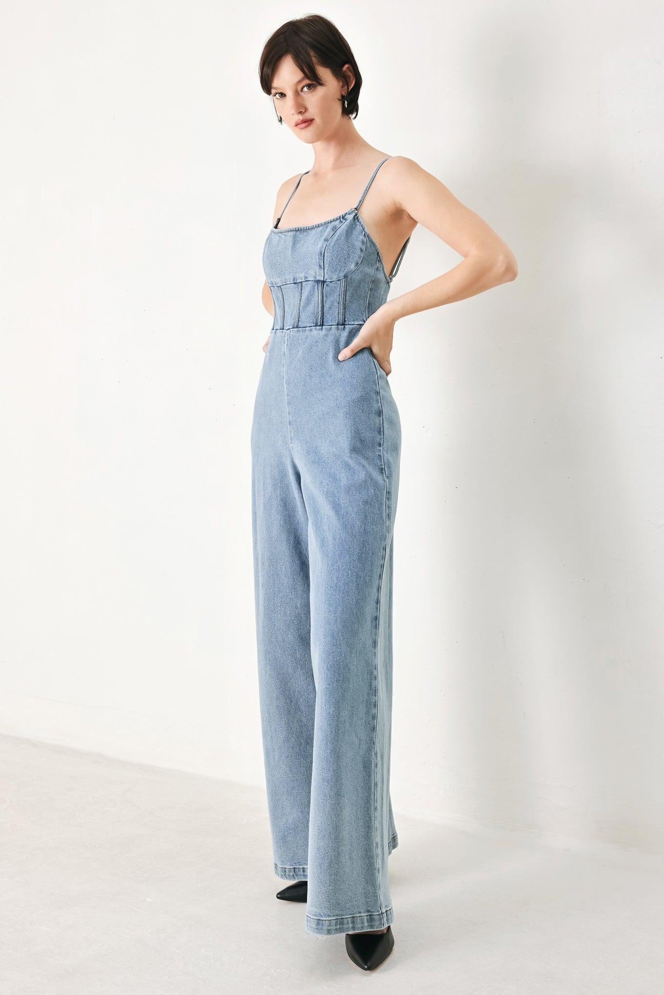 A washed denim jumpsuit featuring U neckline, straps, waist yoke, wide leg, bare back with zipper closure