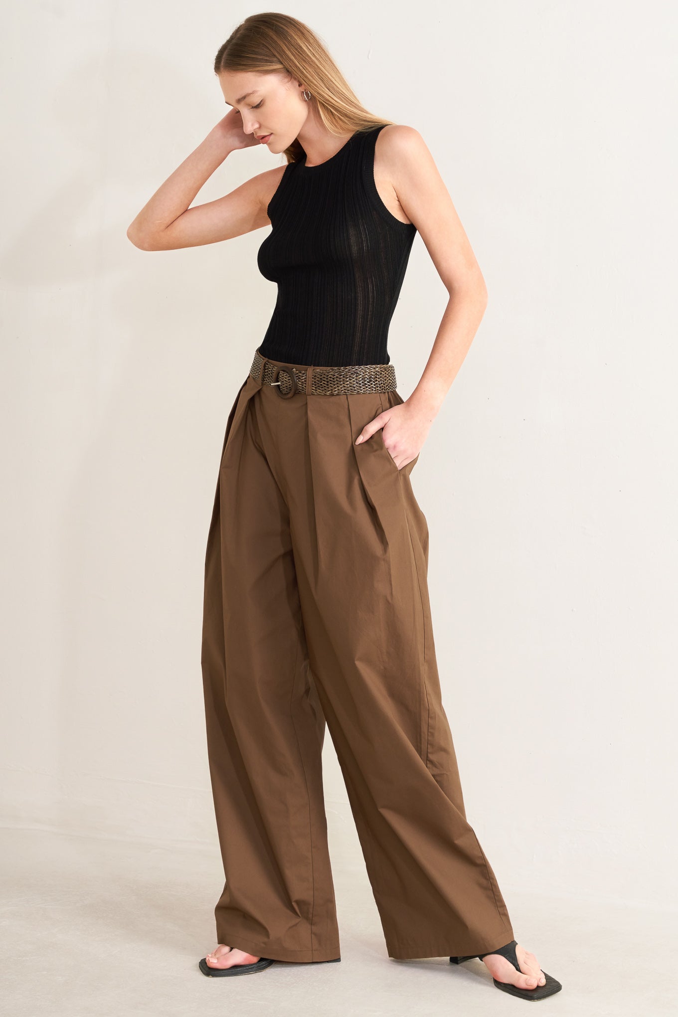 Woman wearing a black sleeveless top and brown wide-leg pants on a plain background