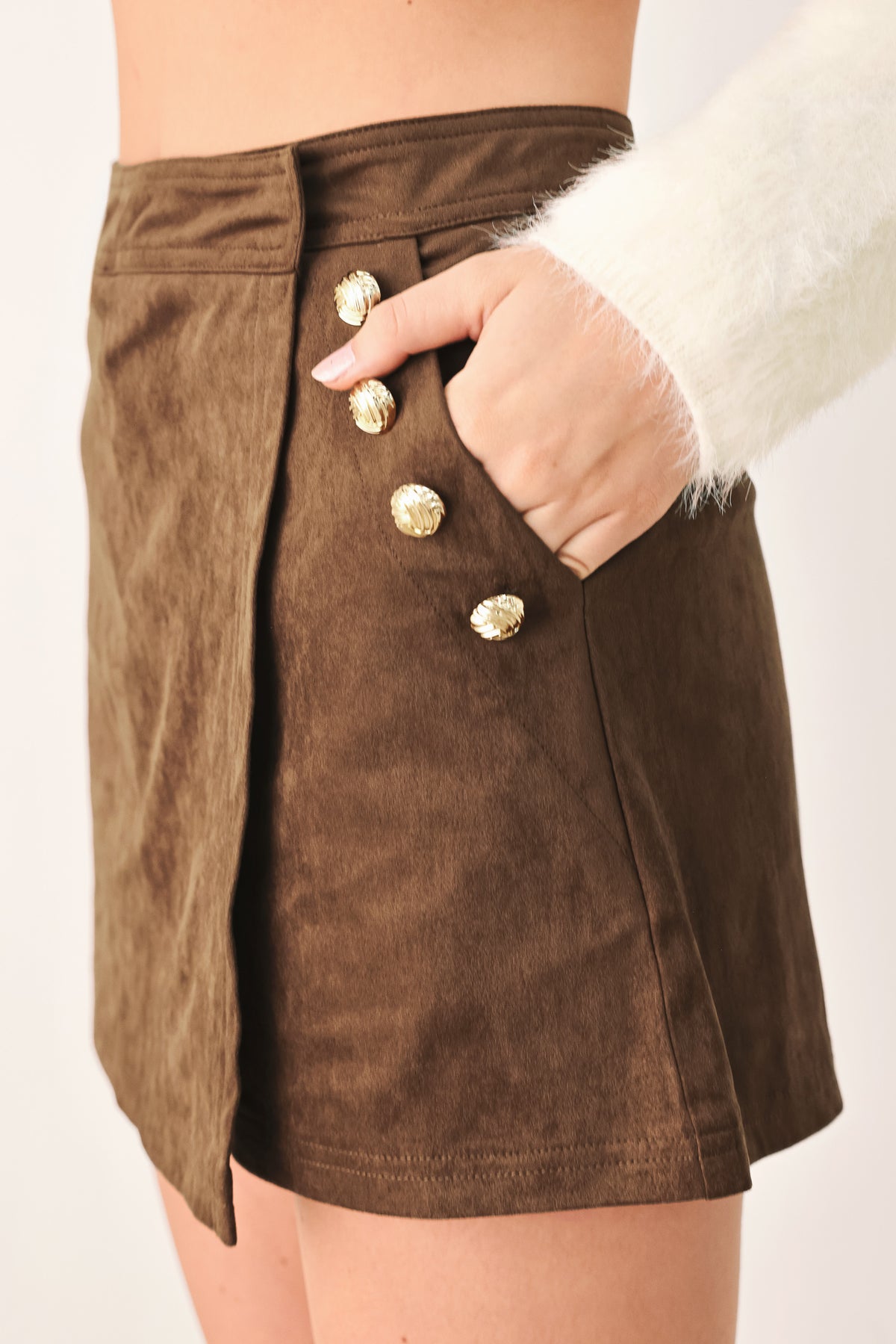 A brown wrap-style mini skort with decorative metallic buttons on the side, shown on a model | FREEMARKET