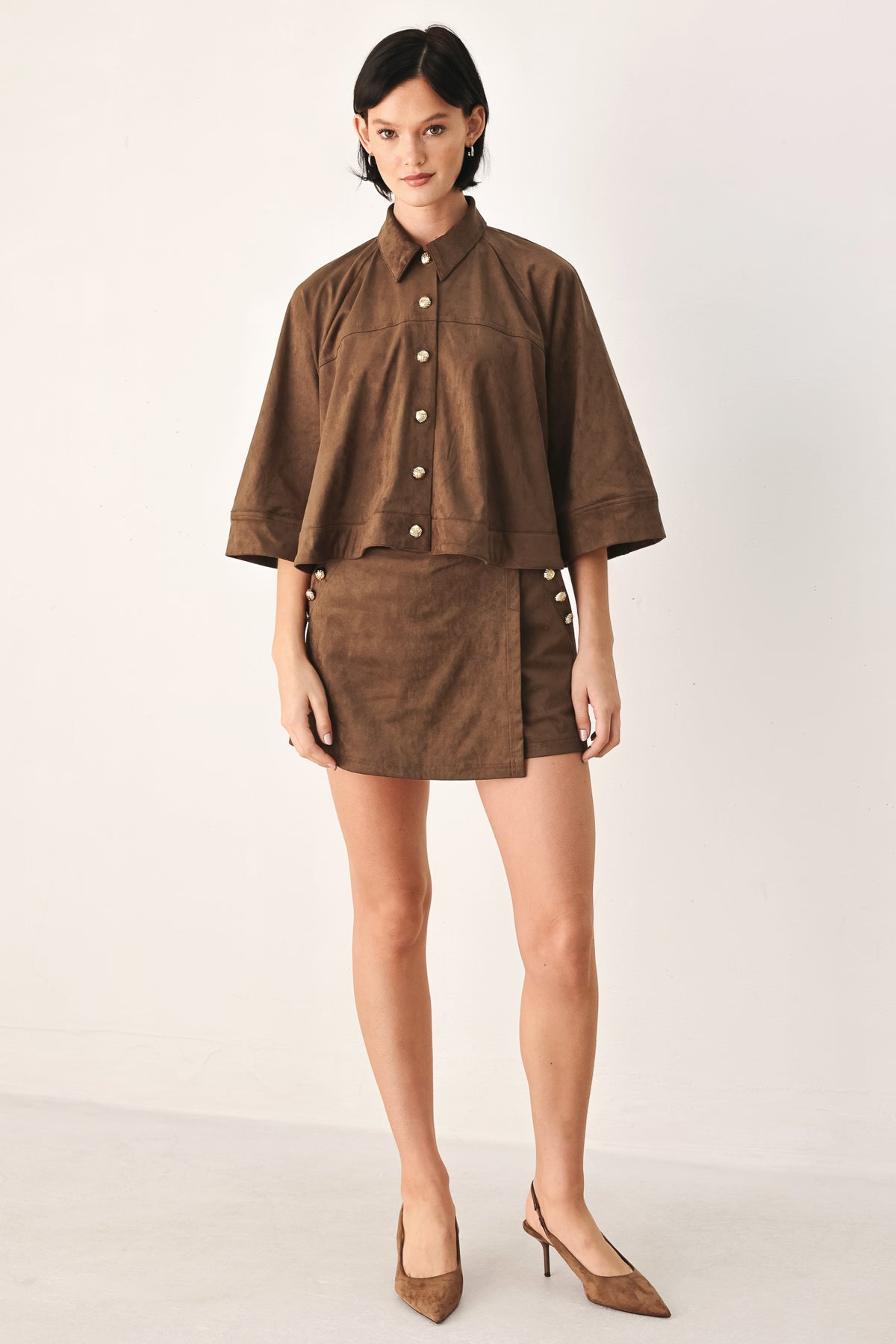 A brown wrap-style mini skort with decorative metallic buttons on the side, shown on a model | FREEMARKET