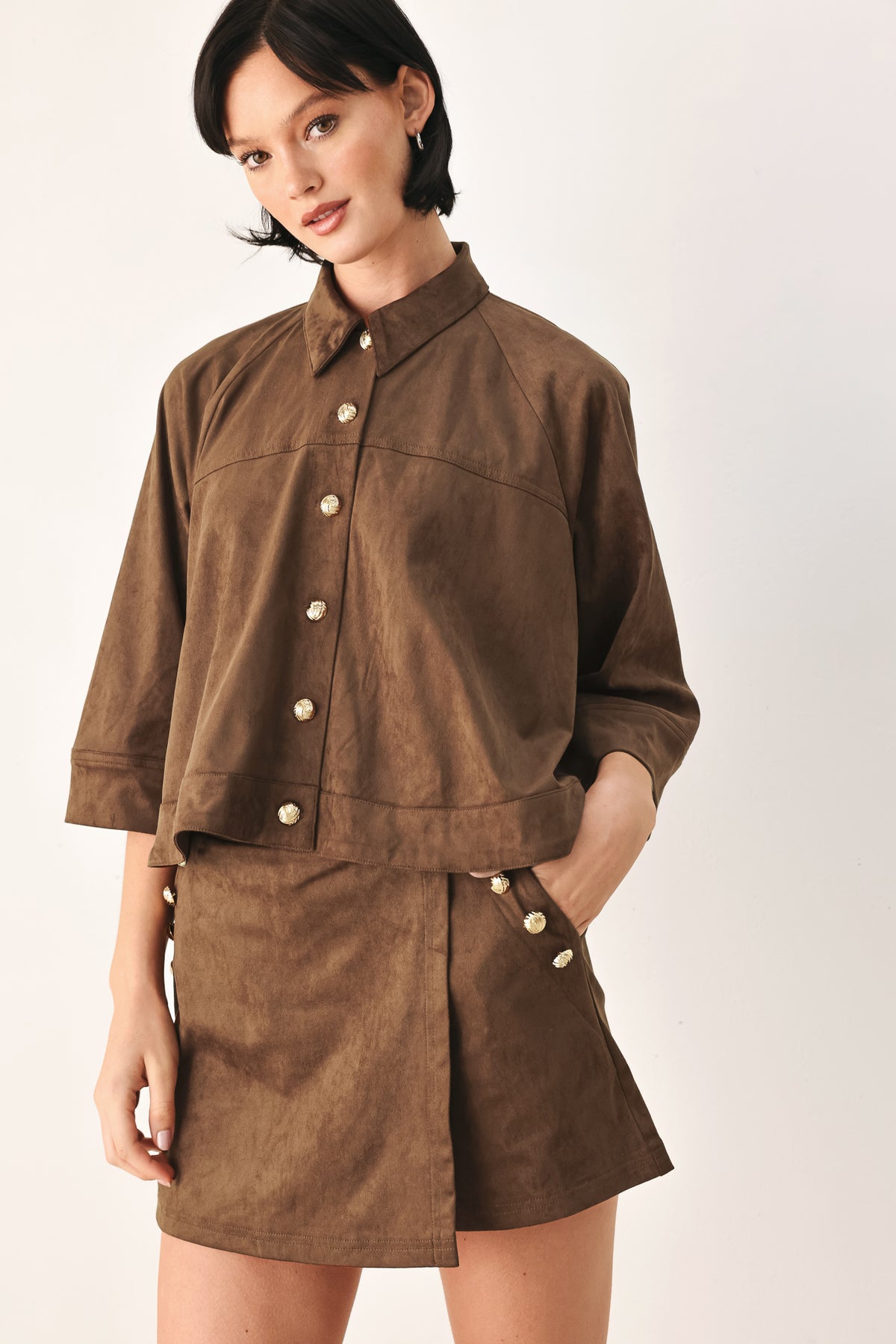 A brown wrap-style mini skort with decorative metallic buttons on the side, shown on a model | FREEMARKET
