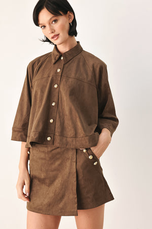 A brown wrap-style mini skort with decorative metallic buttons on the side, shown on a model | FREEMARKET