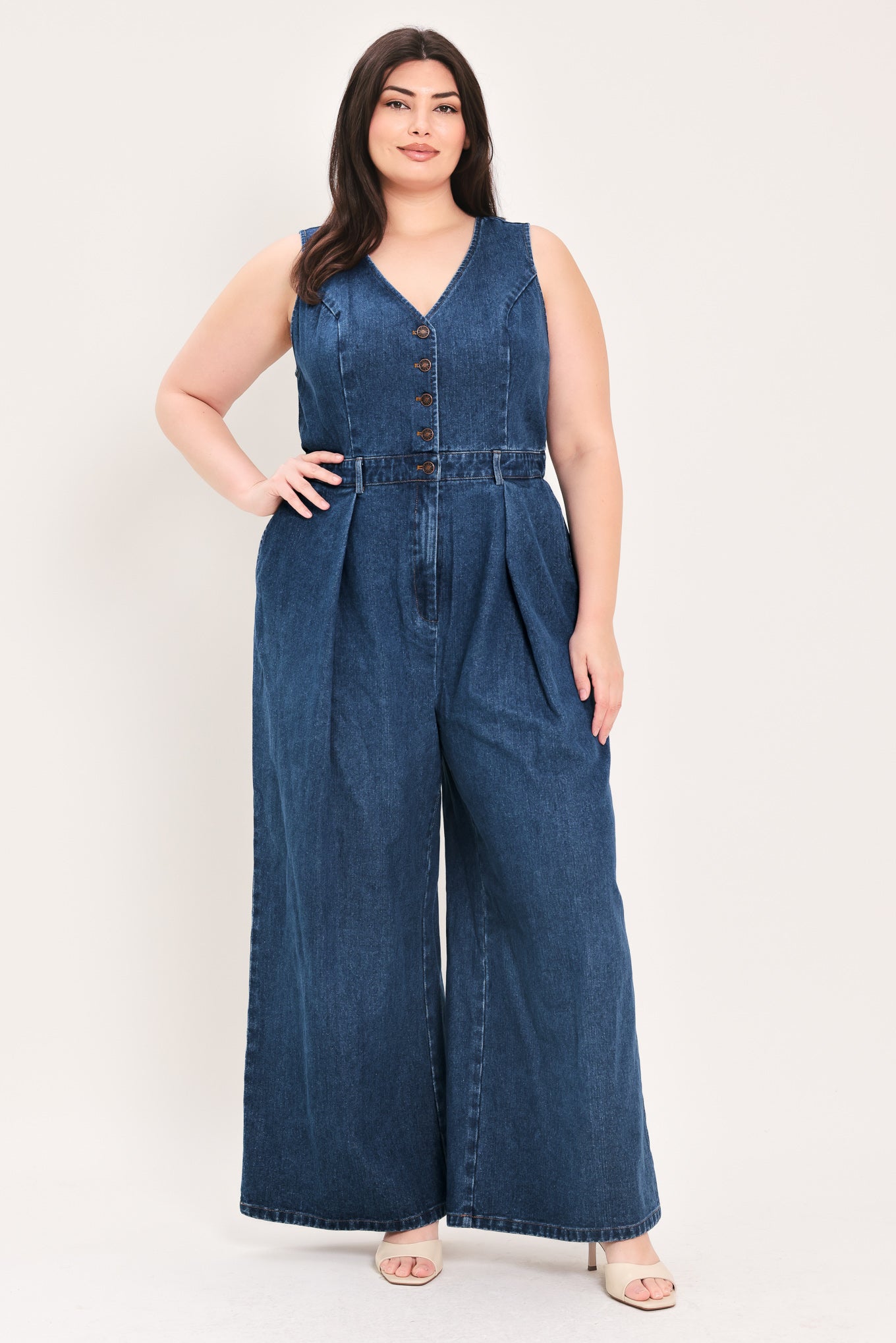 Woman wearing a denim jumpsuit featuring V neckline, sleeveless, front button closure, side pockets, wide leg | FREEMARKET Curve