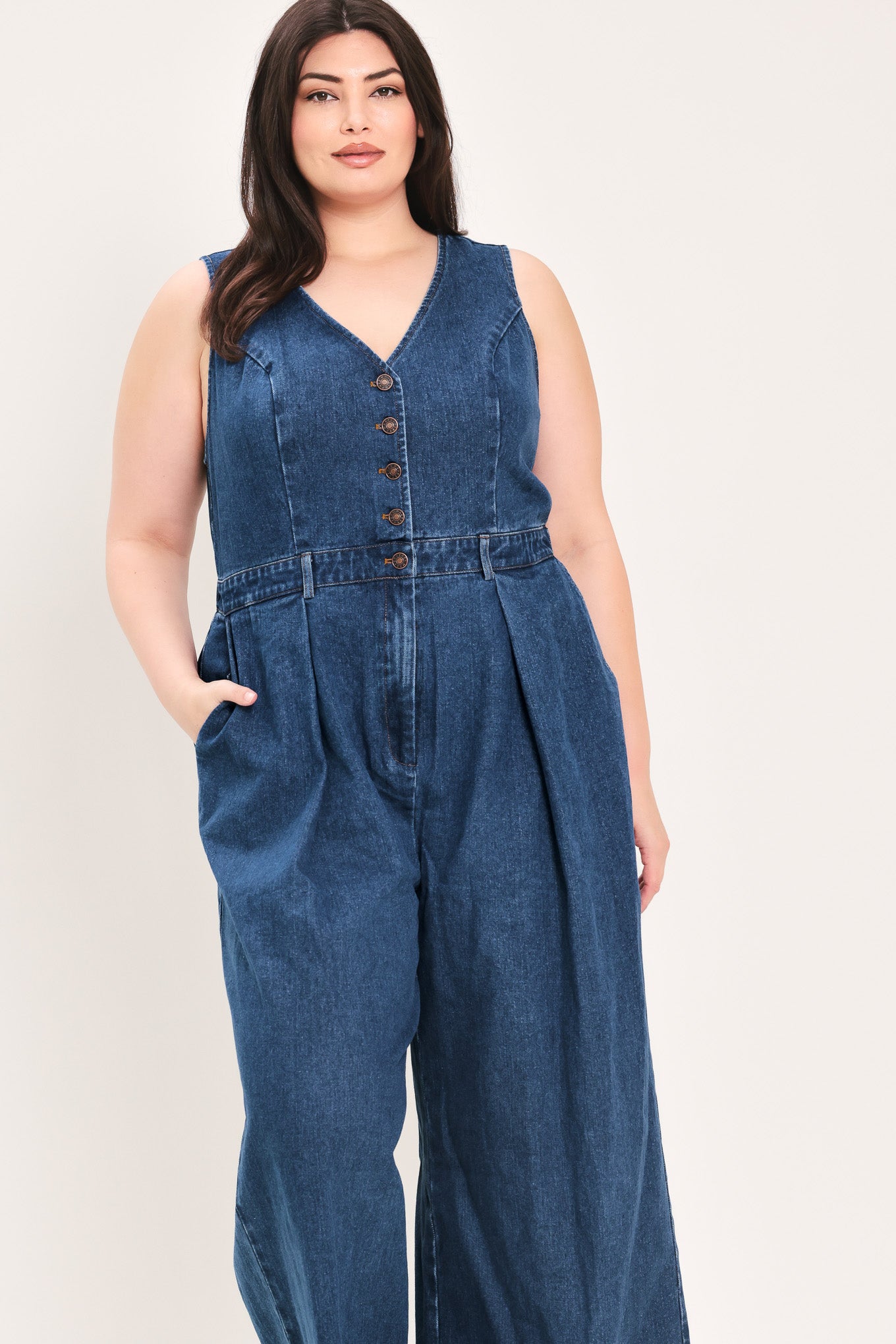 Woman wearing a denim jumpsuit featuring V neckline, sleeveless, front button closure, side pockets, wide leg | FREEMARKET Curve