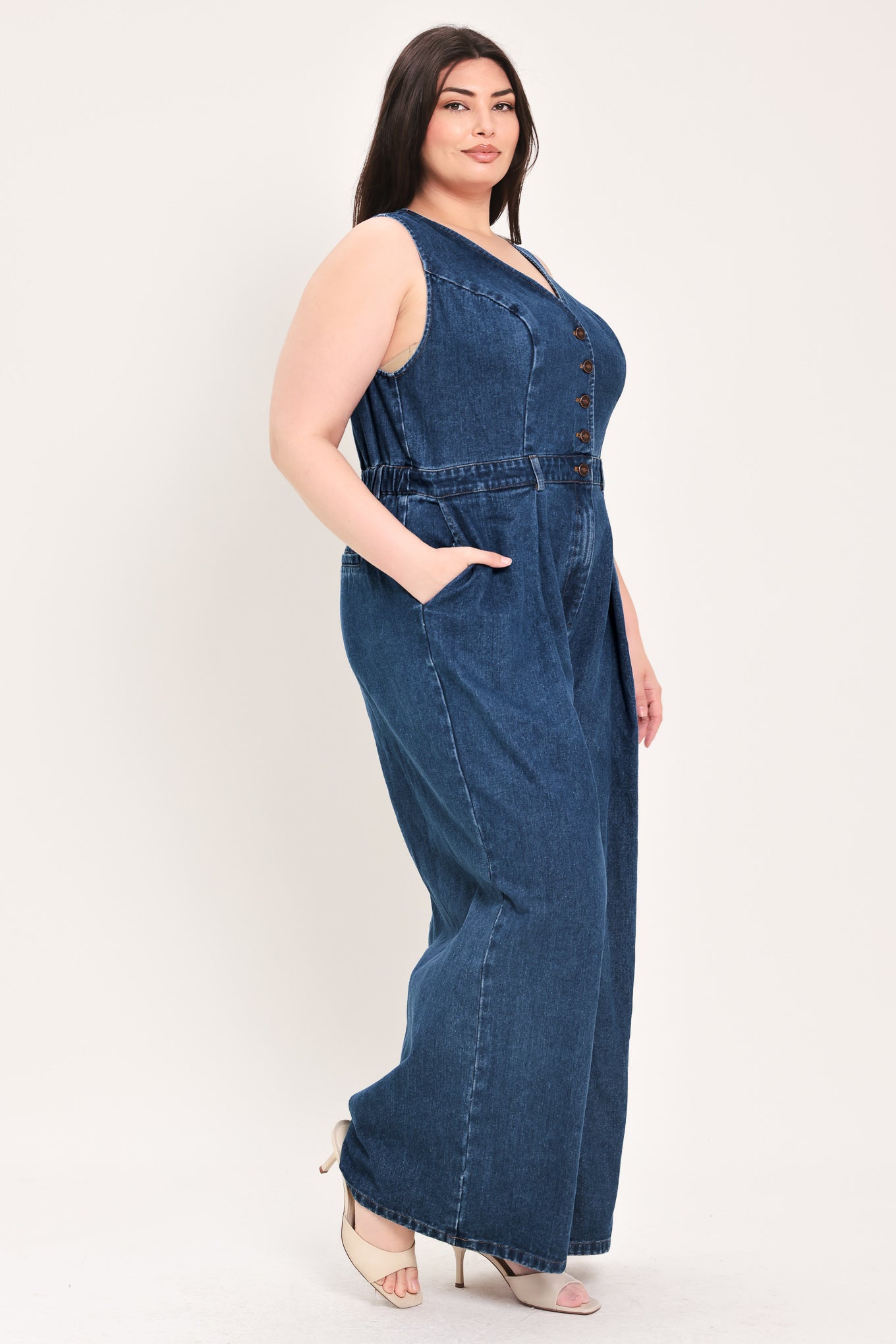 Woman wearing a denim jumpsuit featuring V neckline, sleeveless, front button closure, side pockets, wide leg | FREEMARKET Curve