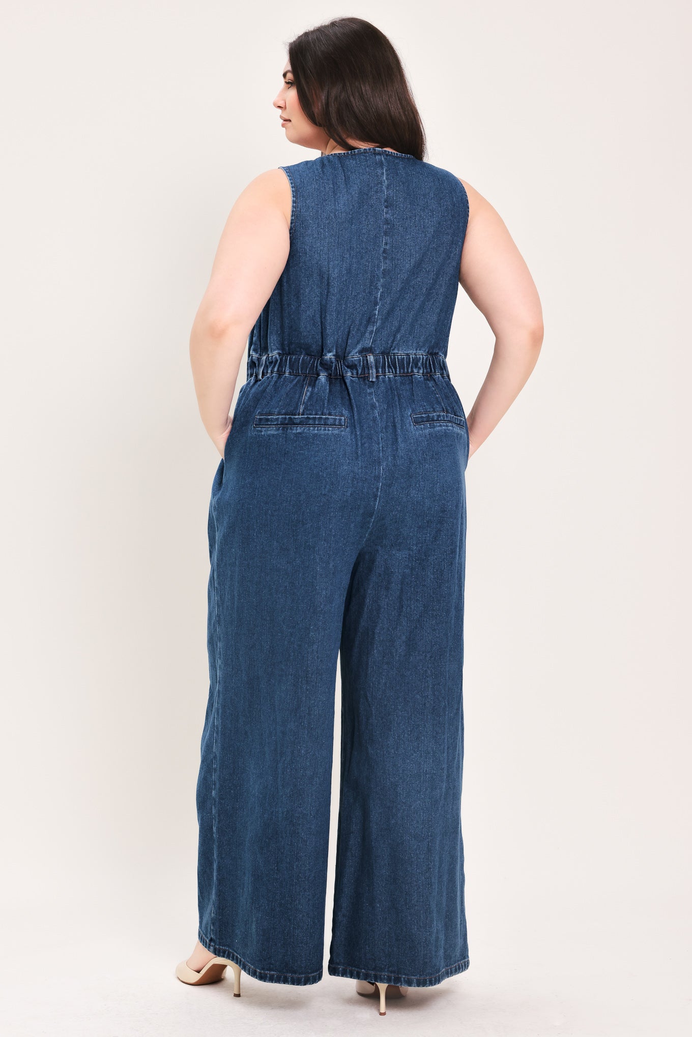 Woman wearing a denim jumpsuit featuring V neckline, sleeveless, front button closure, side pockets, wide leg | FREEMARKET Curve