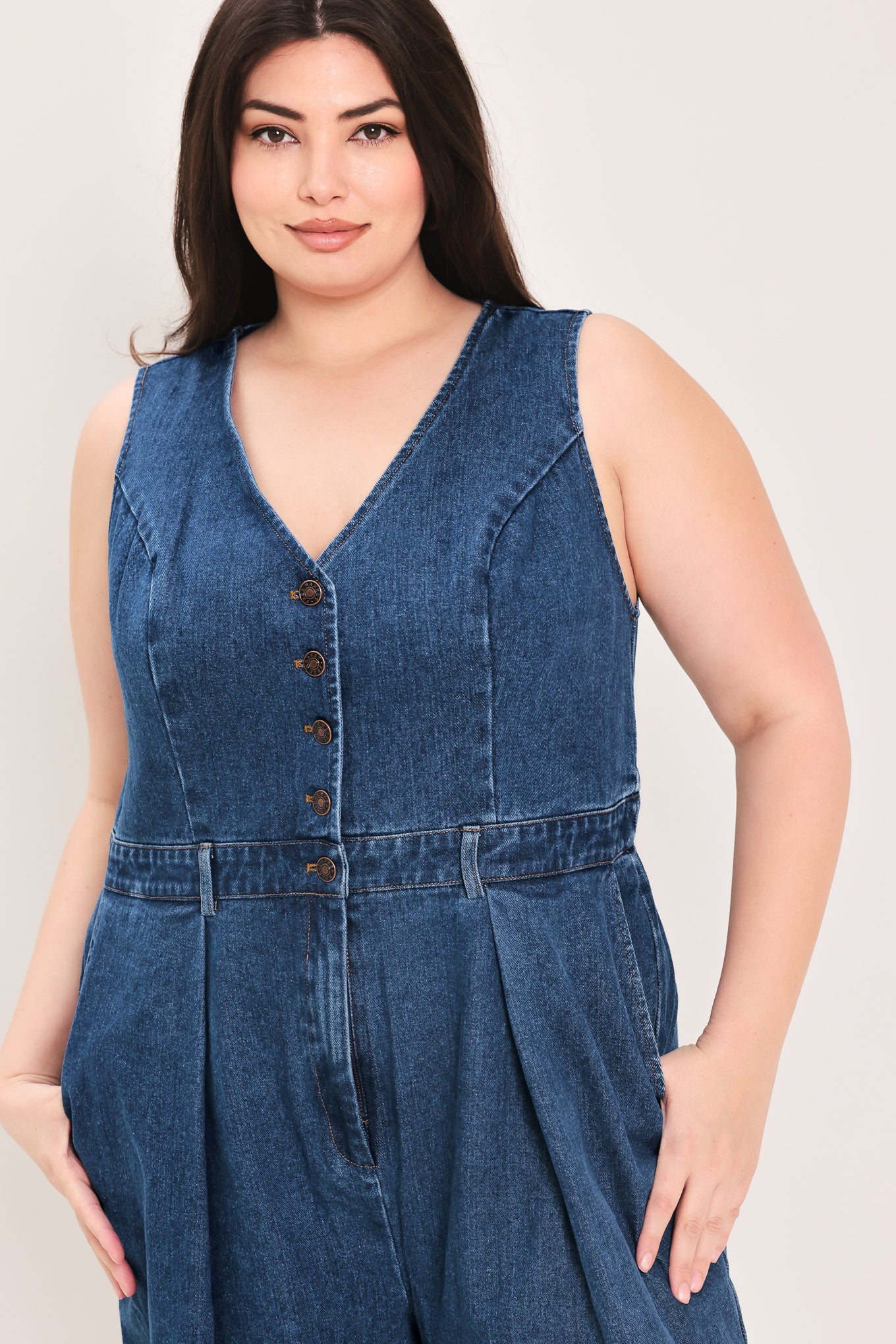 Woman wearing a denim jumpsuit featuring V neckline, sleeveless, front button closure, side pockets, wide leg | FREEMARKET Curve