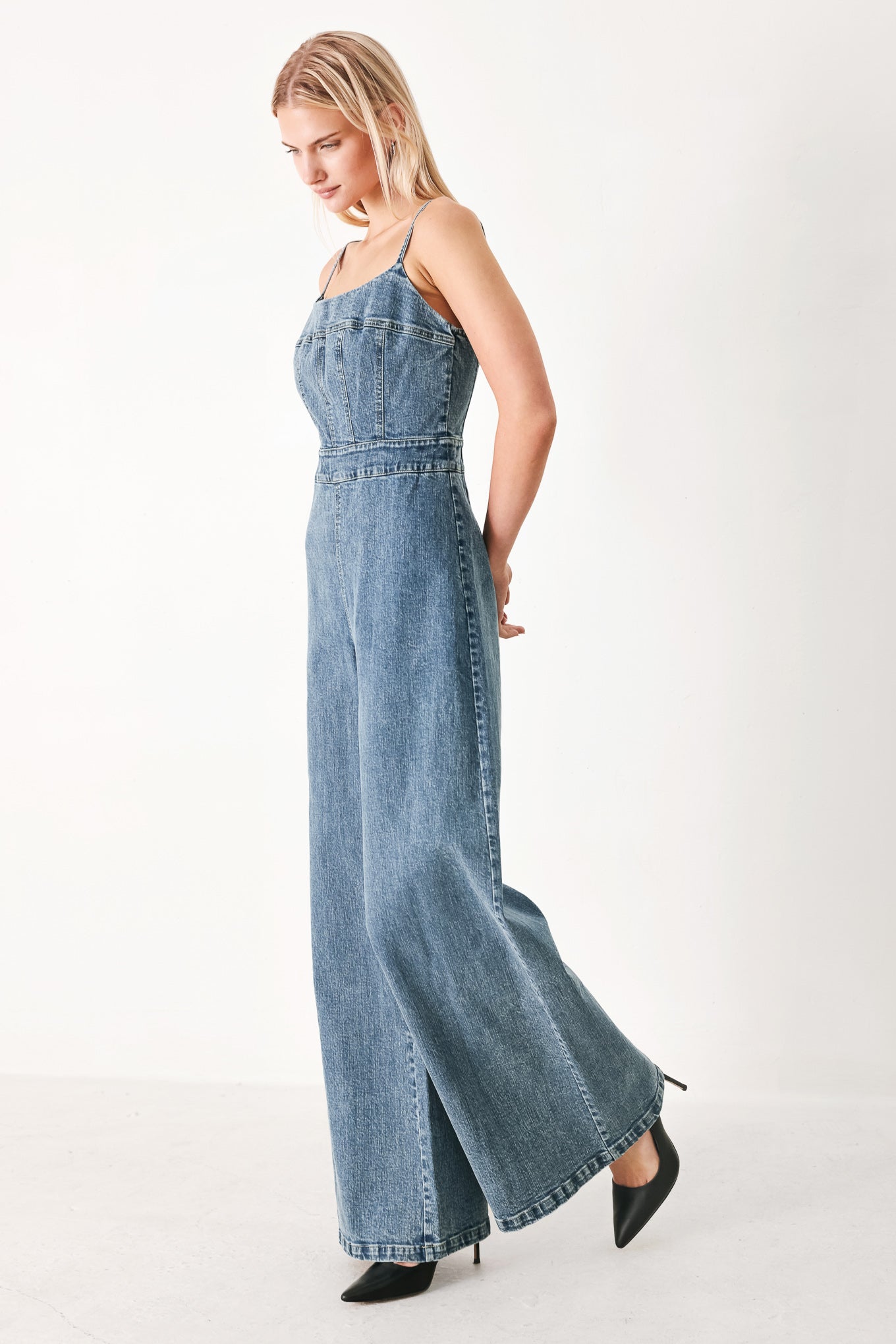 Woman wearing a denim jumpsuit featuring straight neckline, straps, wide leg and back zipper closure | FREEMARKET