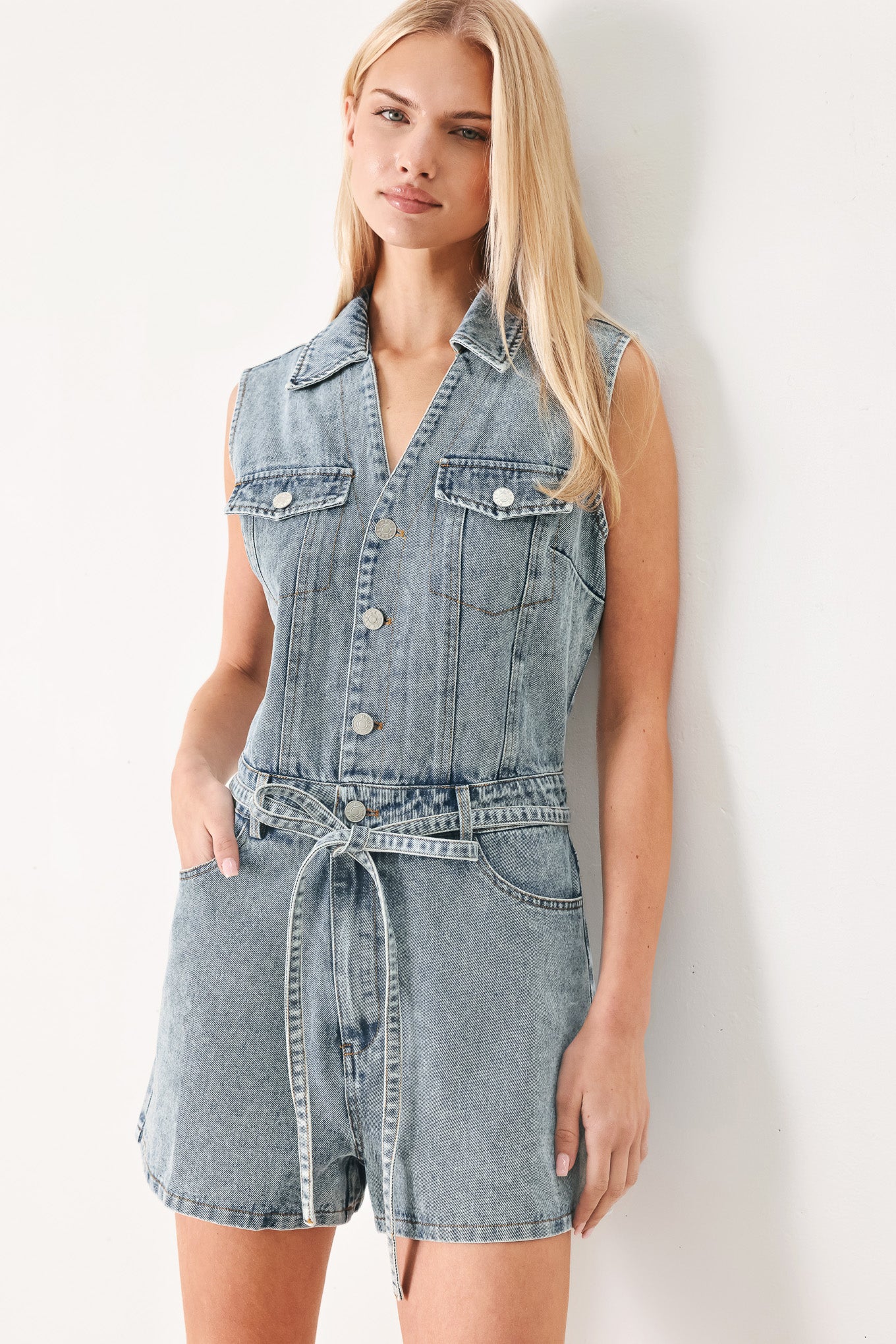 Woman wearing a denim romper with collar, sleeveless, button down, self tie and pockets | FREEMARKET