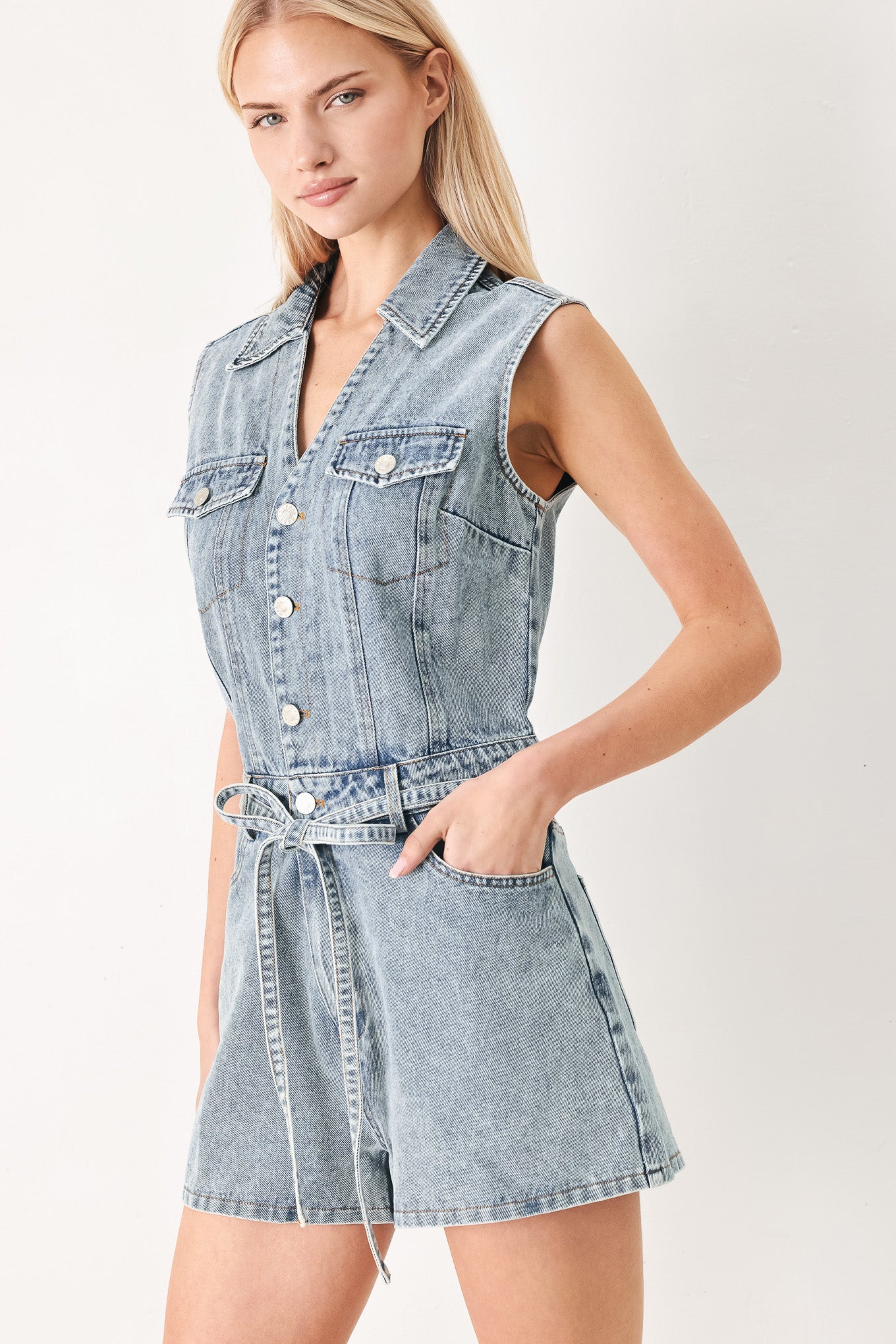 Woman wearing a denim romper with collar, sleeveless, button down, self tie and pockets | FREEMARKET