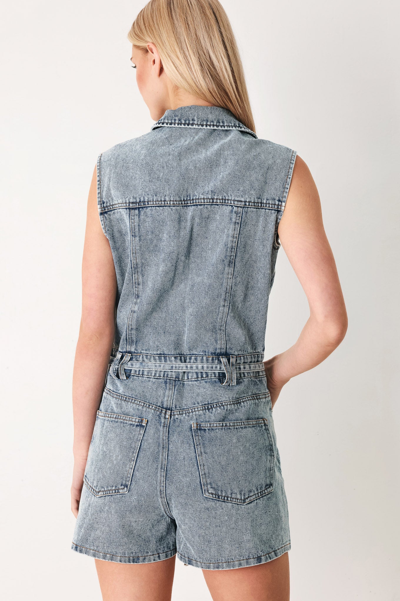 Woman wearing a denim romper with collar, sleeveless, button down, self tie and pockets | FREEMARKET