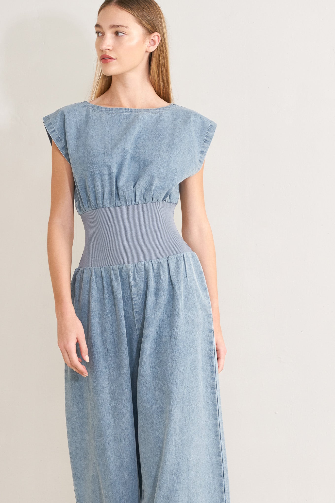 Woman wearing a denim jumpsuit featuring wide neckline, short sleeve, wide knit waistband, wide leg and back slit with button closure | FREEMARKET