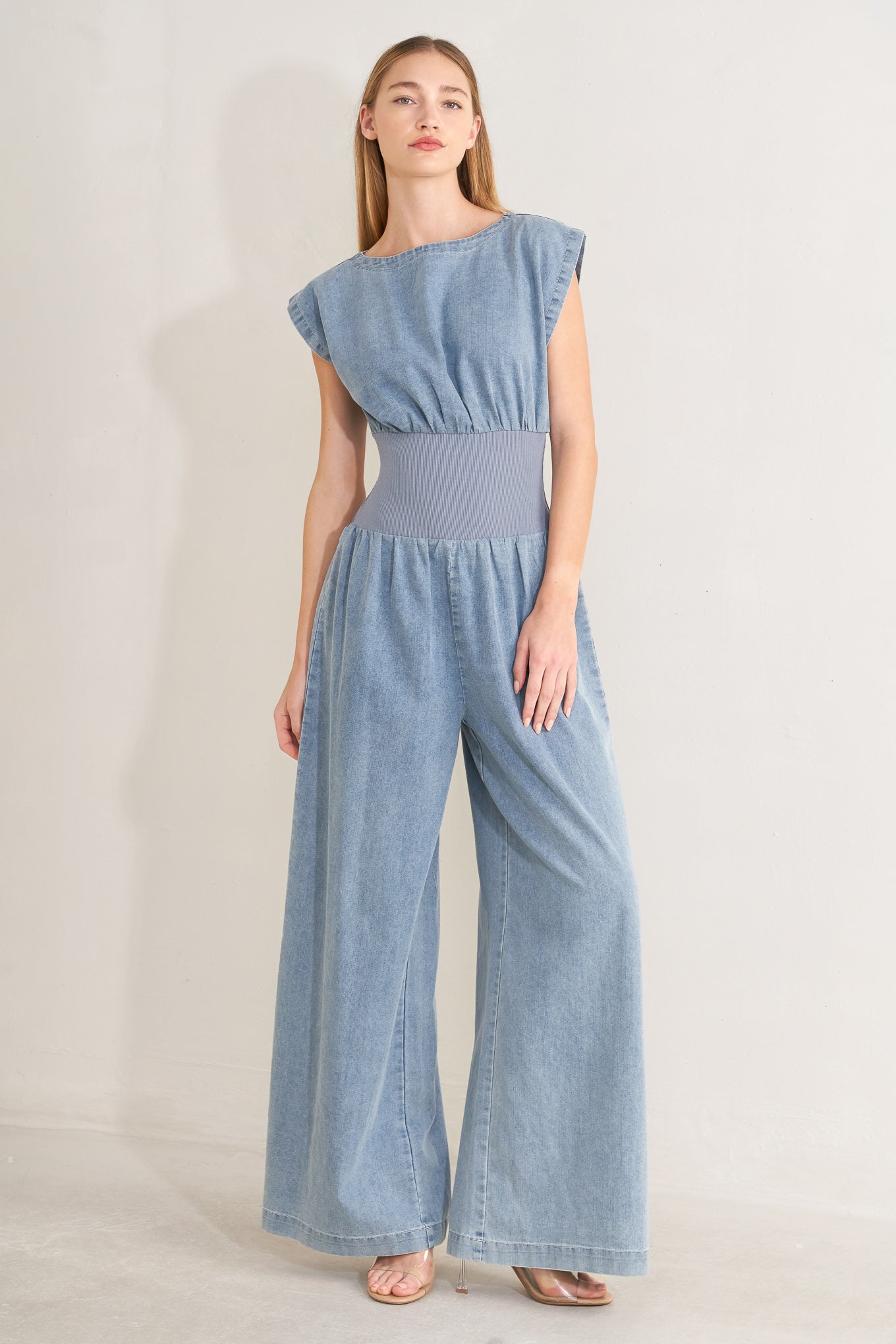 Woman wearing a denim jumpsuit featuring wide neckline, short sleeve, wide knit waistband, wide leg and back slit with button closure | FREEMARKET