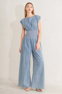 Woman wearing a denim jumpsuit featuring wide neckline, short sleeve, wide knit waistband, wide leg and back slit with button closure | FREEMARKET