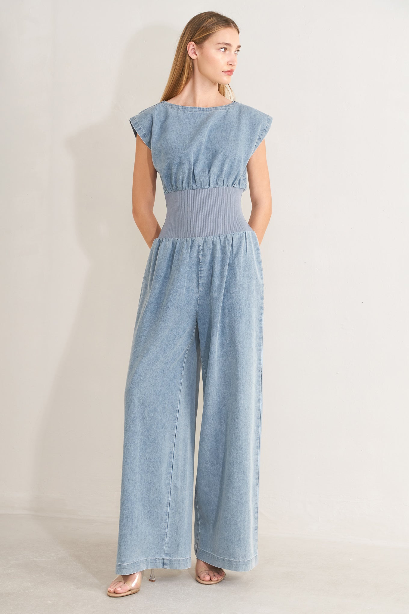 Woman wearing a denim jumpsuit featuring wide neckline, short sleeve, wide knit waistband, wide leg and back slit with button closure | FREEMARKET