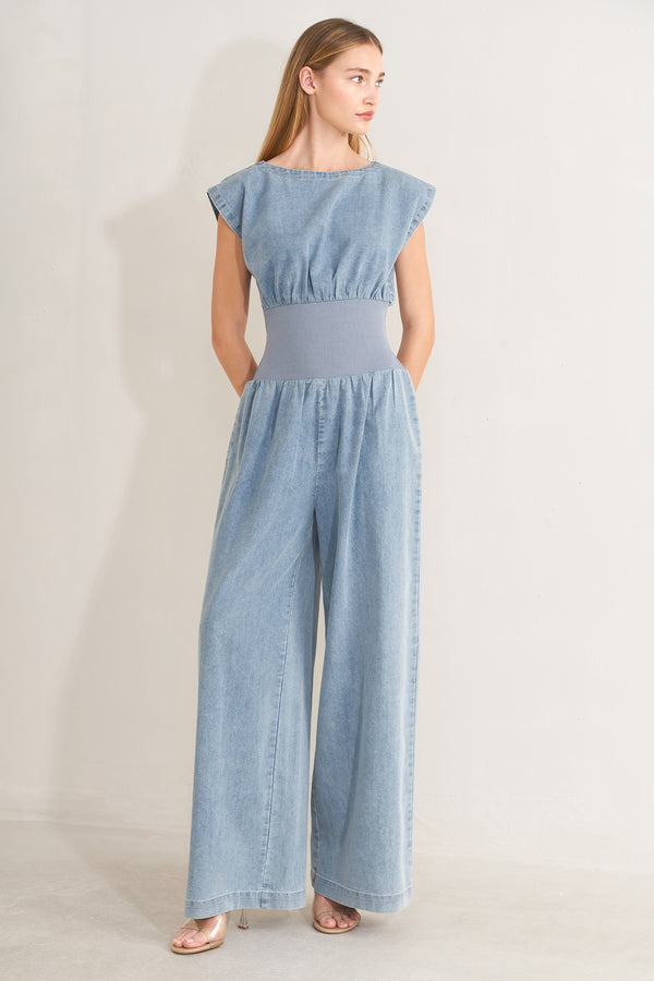 Woman wearing a denim jumpsuit featuring wide neckline, short sleeve, wide knit waistband, wide leg and back slit with button closure | FREEMARKET