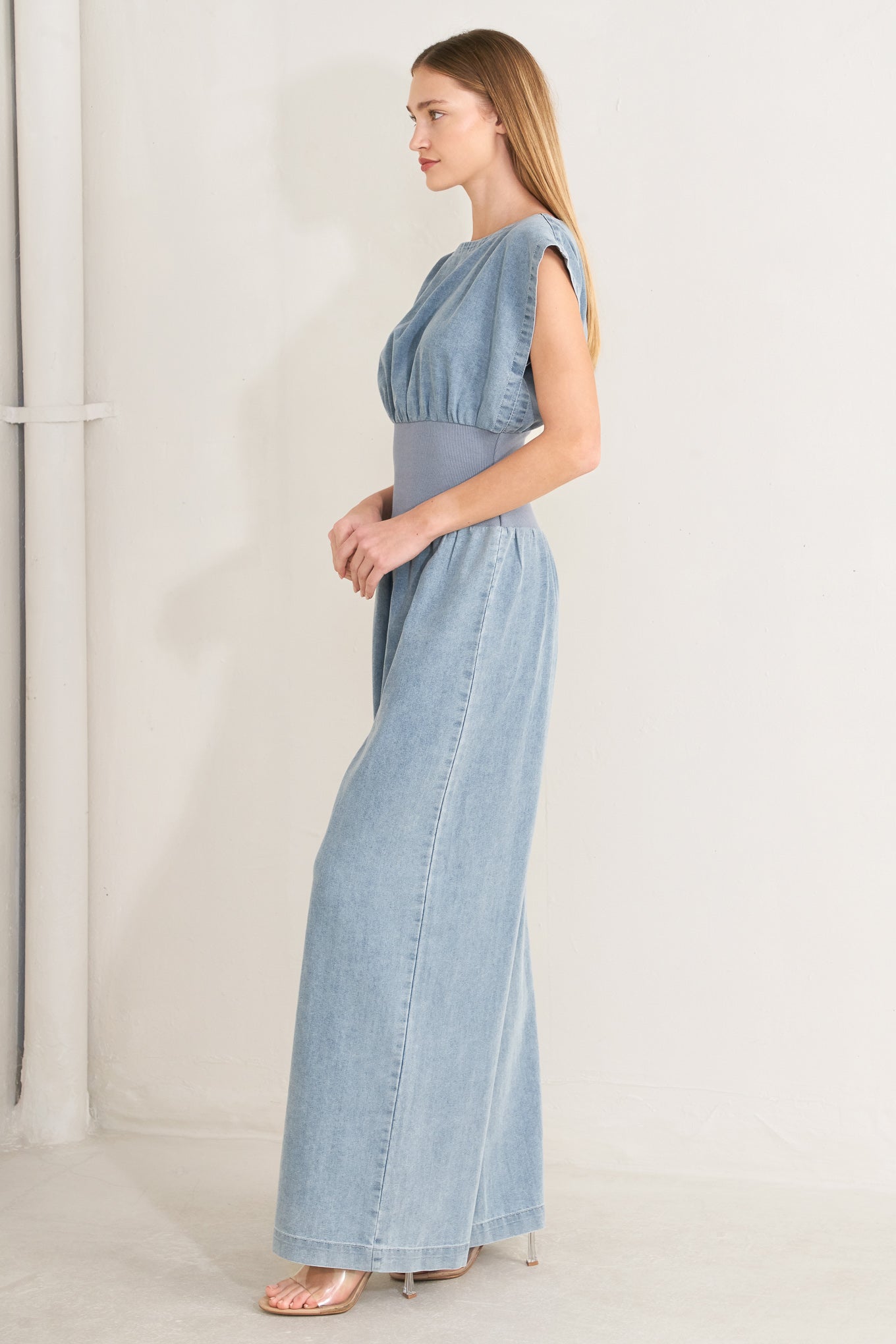 Woman wearing a denim jumpsuit featuring wide neckline, short sleeve, wide knit waistband, wide leg and back slit with button closure | FREEMARKET