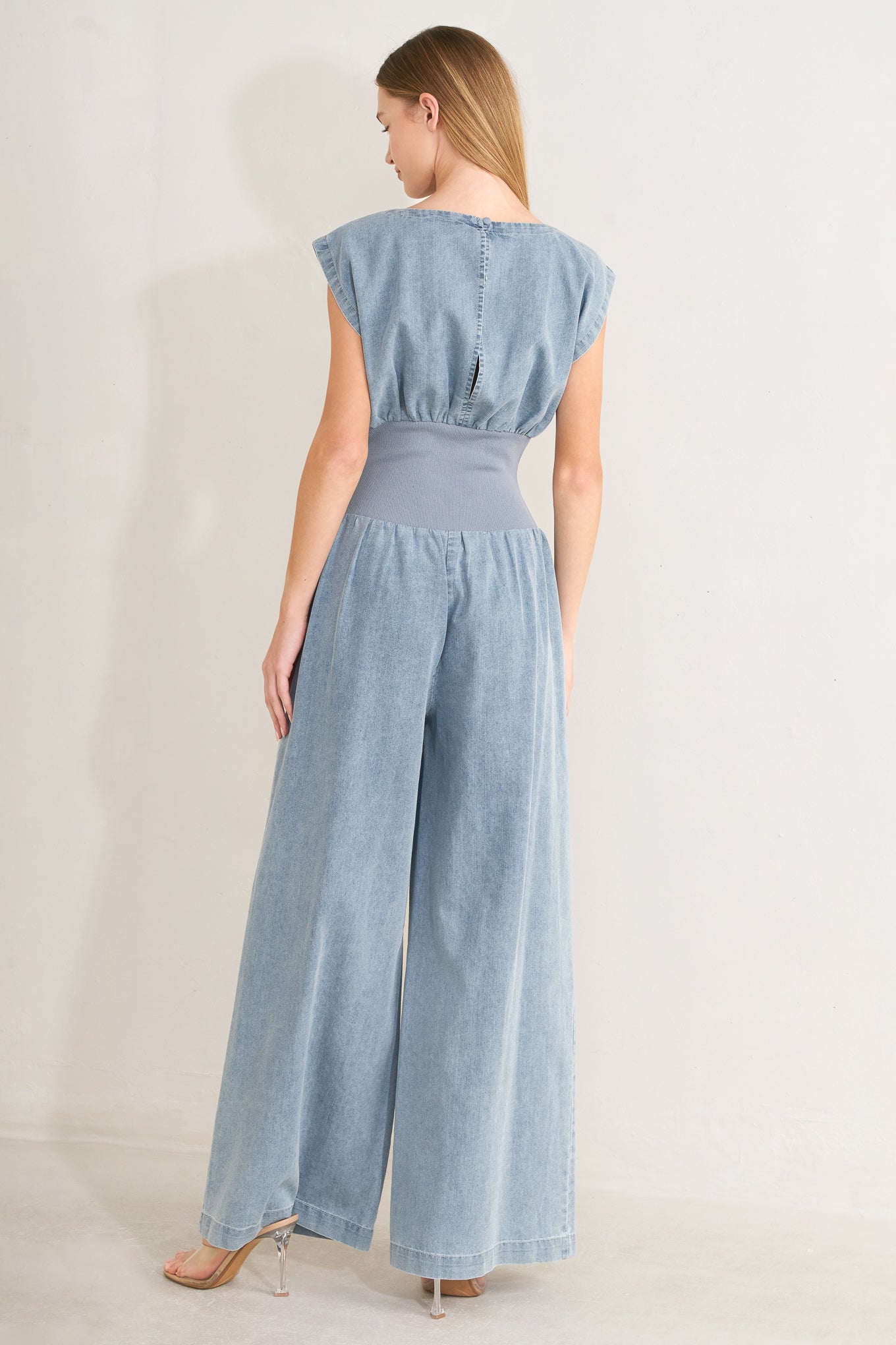 Woman wearing a denim jumpsuit featuring wide neckline, short sleeve, wide knit waistband, wide leg and back slit with button closure | FREEMARKET