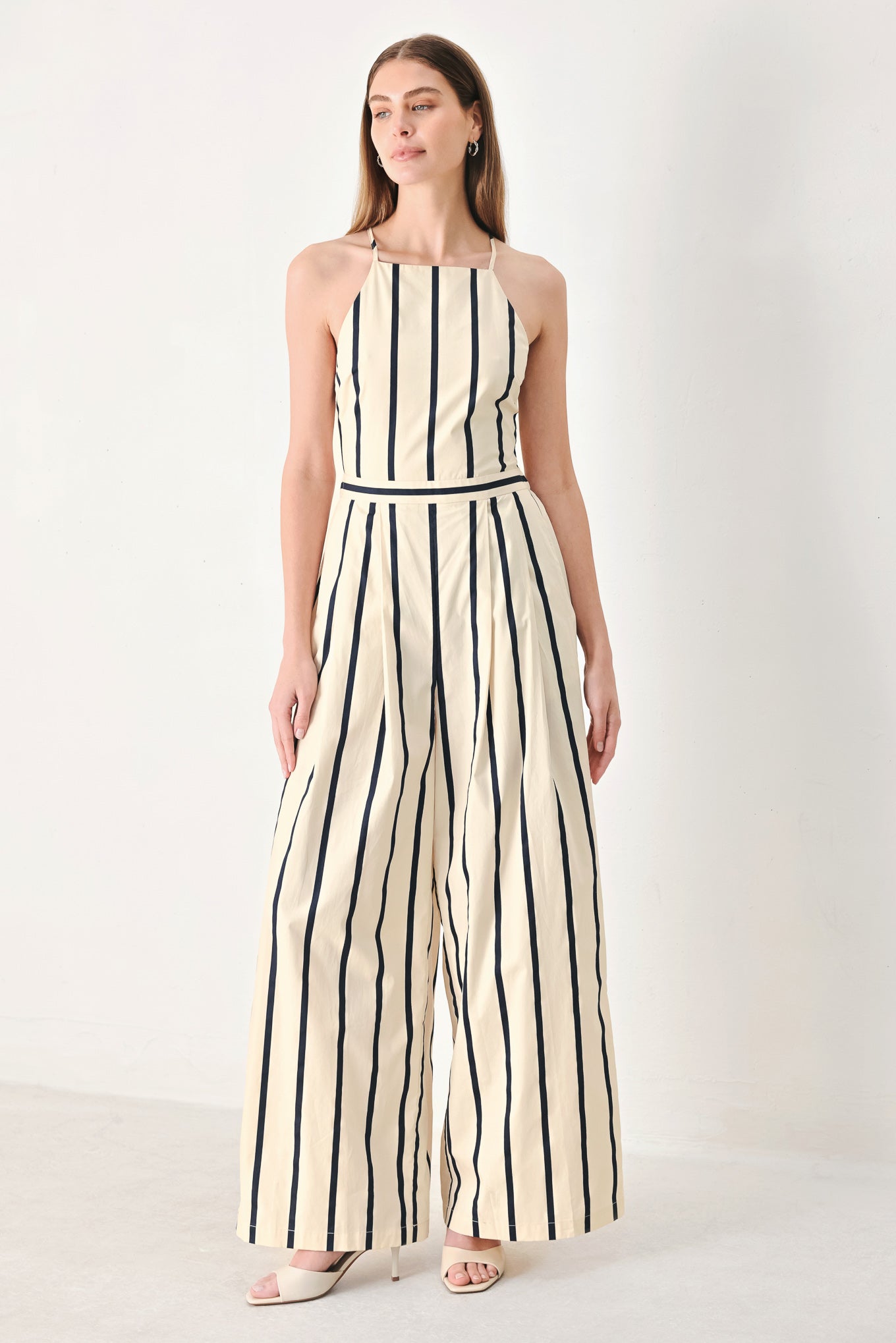 Woman wearing a navy and ivory striped  jumpsuit featuring straight neckline, side pockets, bare back with tie and wide leg | FREEMARKET | Flying Tomato