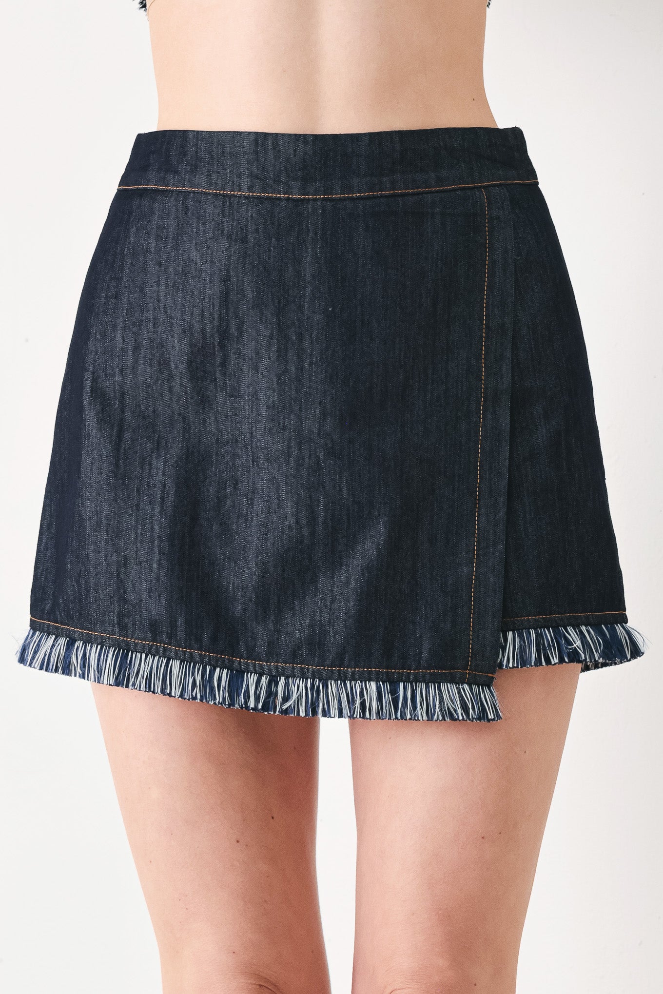 Woman wearing a dark denim skort featuring front flap, fray edge and back zipper closure | FREEMARKET