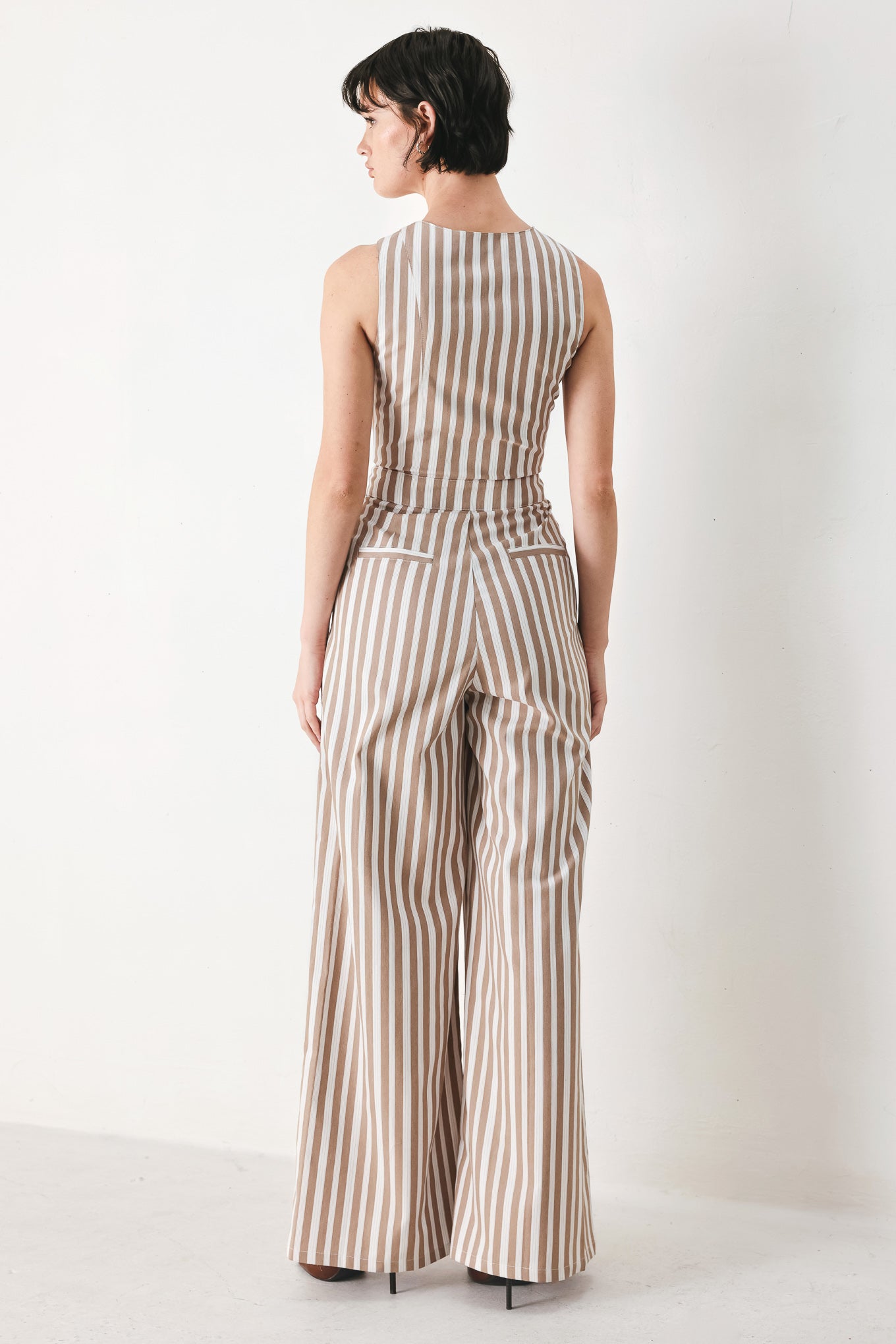 Woman wearing a striped woven jumpsuit featuring V neckline, sleeveless, front button/zipper closure and wide leg | FREEMARKET