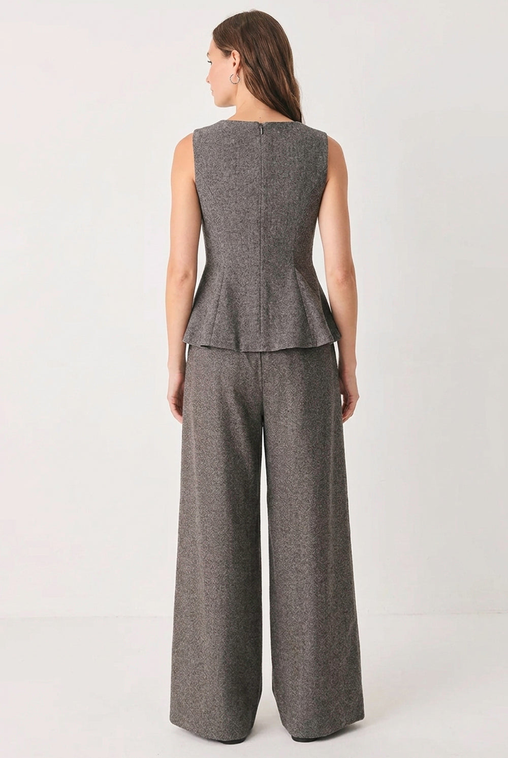 A woman wearing taupe-gray wide-leg pants stands in a styled room holding a laptop, with a clothing rack and fashion magazine pages in the background | FREEMARKET