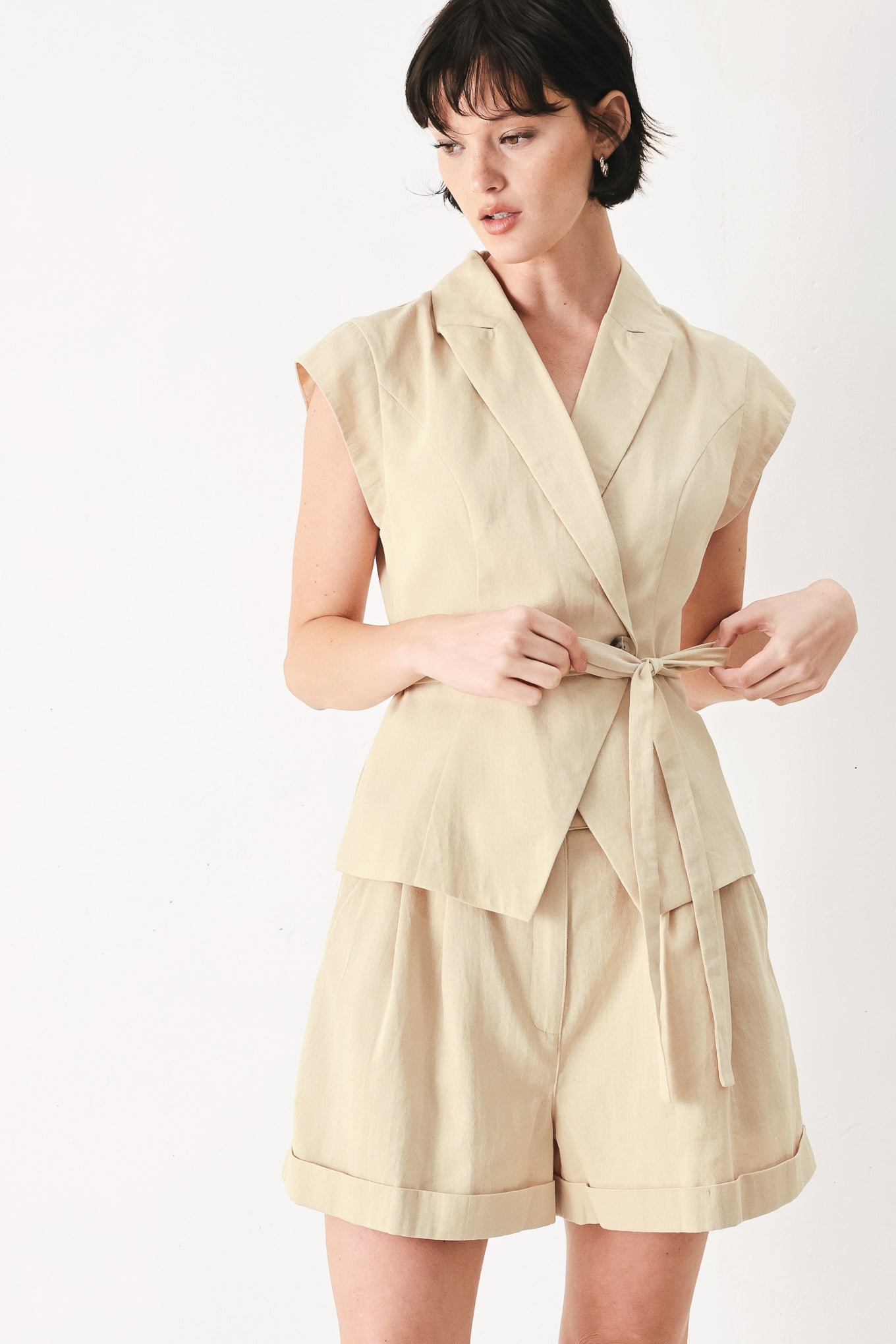 Woman wearing light beige woven shorts with front closure, pockets and cuff hem | FEEMARKET