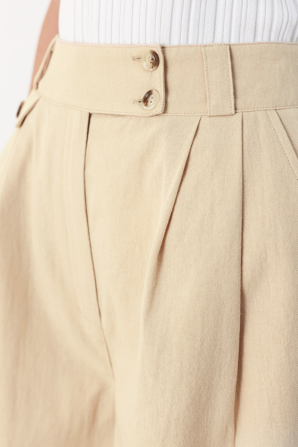 Woman wearing light beige woven shorts with front closure, pockets and cuff hem | FEEMARKET