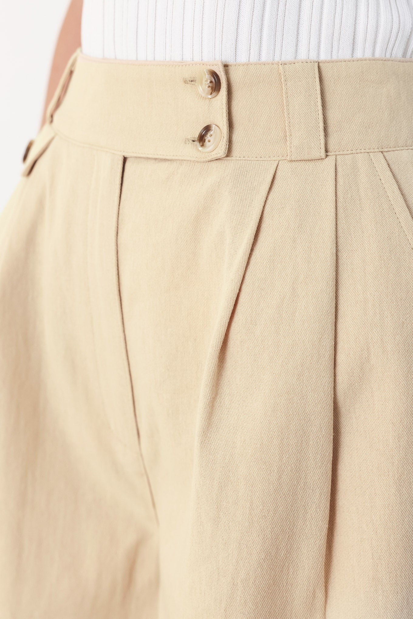 Woman wearing light beige woven shorts with front closure, pockets and cuff hem | FEEMARKET