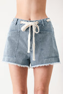 Woman wearing denim shorts with front closure, side pockets, contrasting tie with grommet and fray hem | FREEMARKET