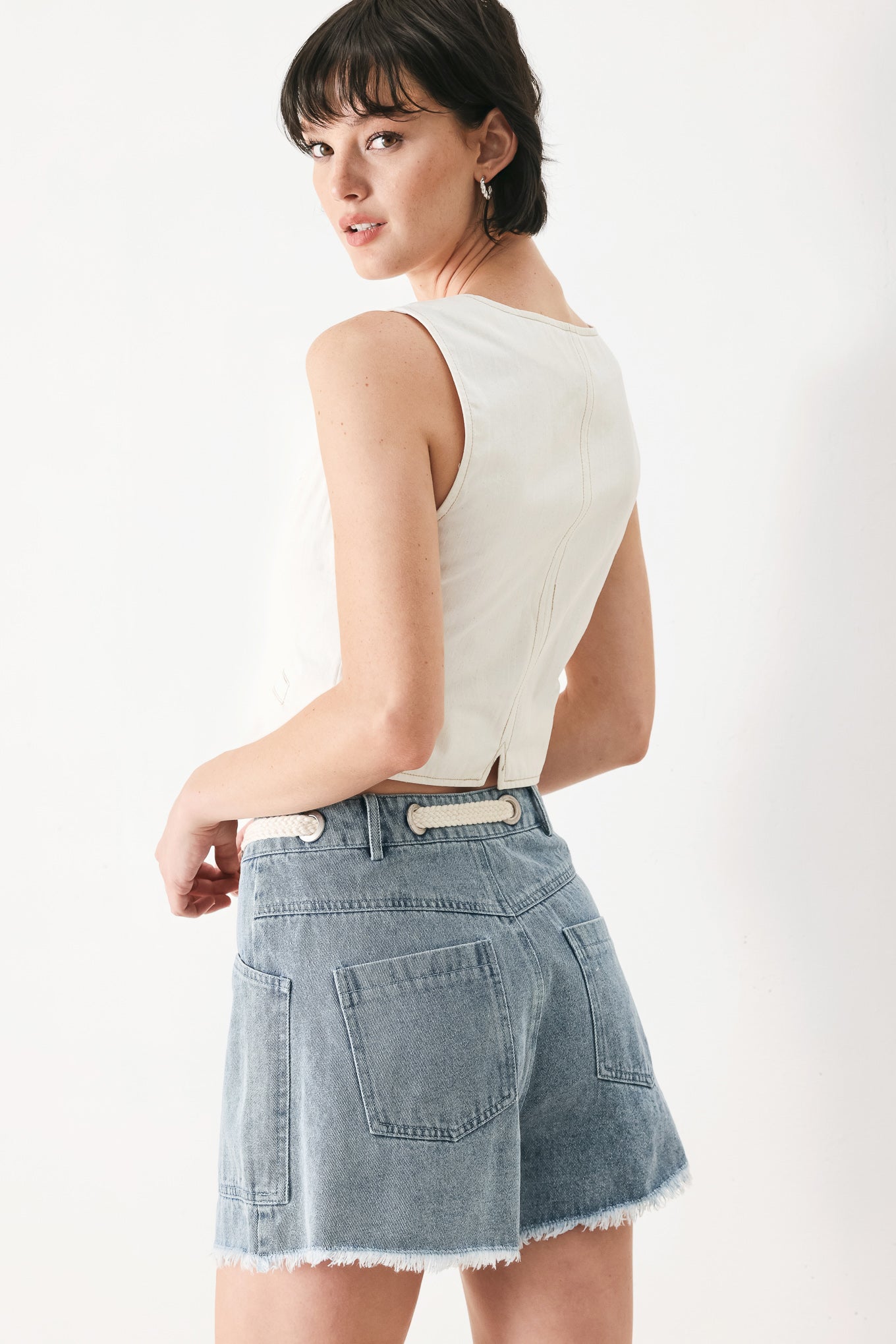 Woman wearing denim shorts with front closure, side pockets, contrasting tie with grommet and fray hem | FREEMARKET