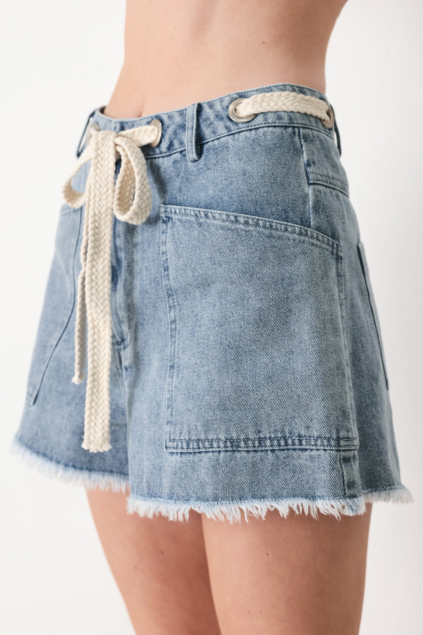 Woman wearing denim shorts with front closure, side pockets, contrasting tie with grommet and fray hem | FREEMARKET