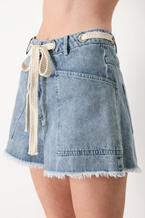 Woman wearing denim shorts with front closure, side pockets, contrasting tie with grommet and fray hem | FREEMARKET
