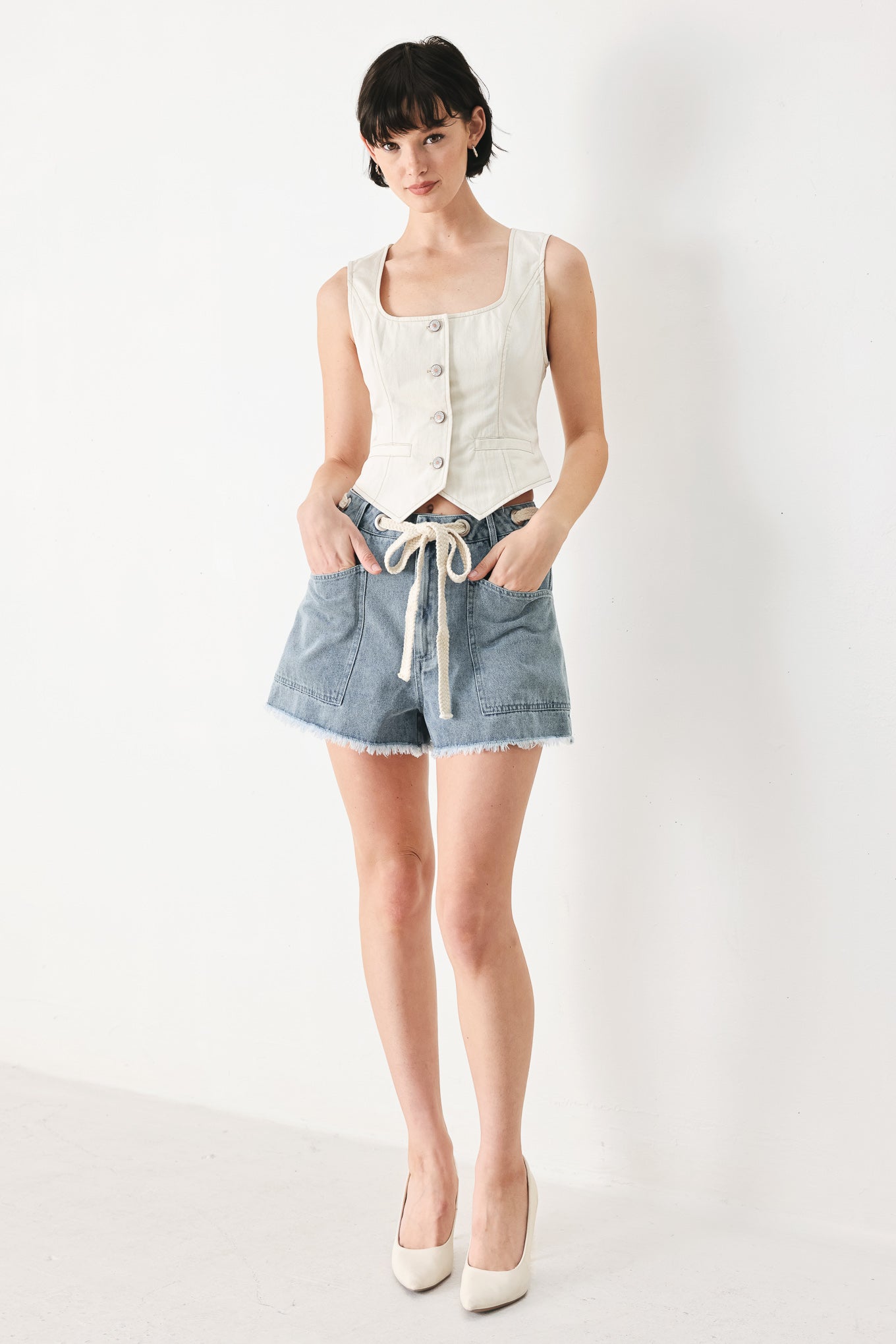 Woman wearing denim shorts with front closure, side pockets, contrasting tie with grommet and fray hem | FREEMARKET