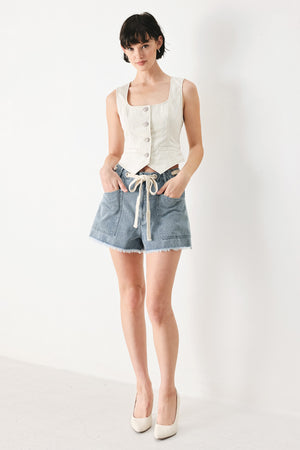 Woman wearing denim shorts with front closure, side pockets, contrasting tie with grommet and fray hem | FREEMARKET