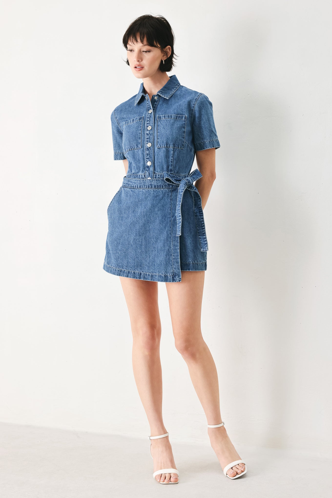 Woman wearing a blue denim skort romper featuring front closure, short sleeve, pockets and side tie | FREEMARKET