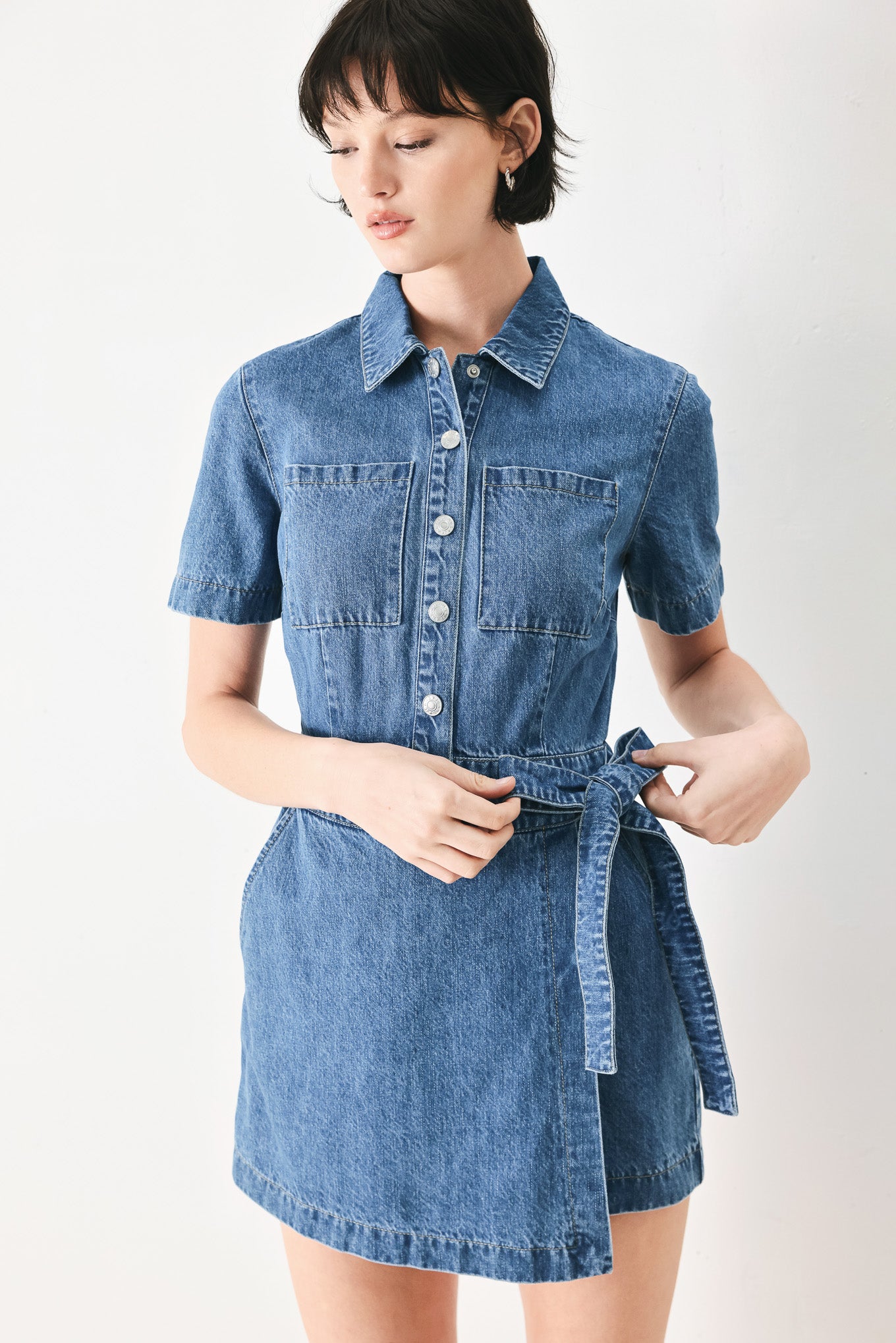 Woman wearing a blue denim skort romper featuring front closure, short sleeve, pockets and side tie | FREEMARKET