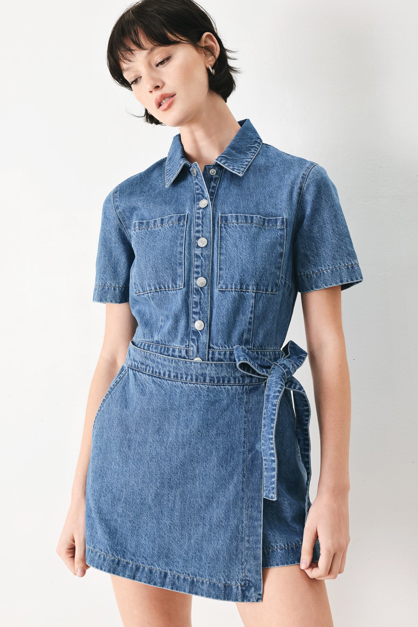 Woman wearing a blue denim skort romper featuring front closure, short sleeve, pockets and side tie | FREEMARKET