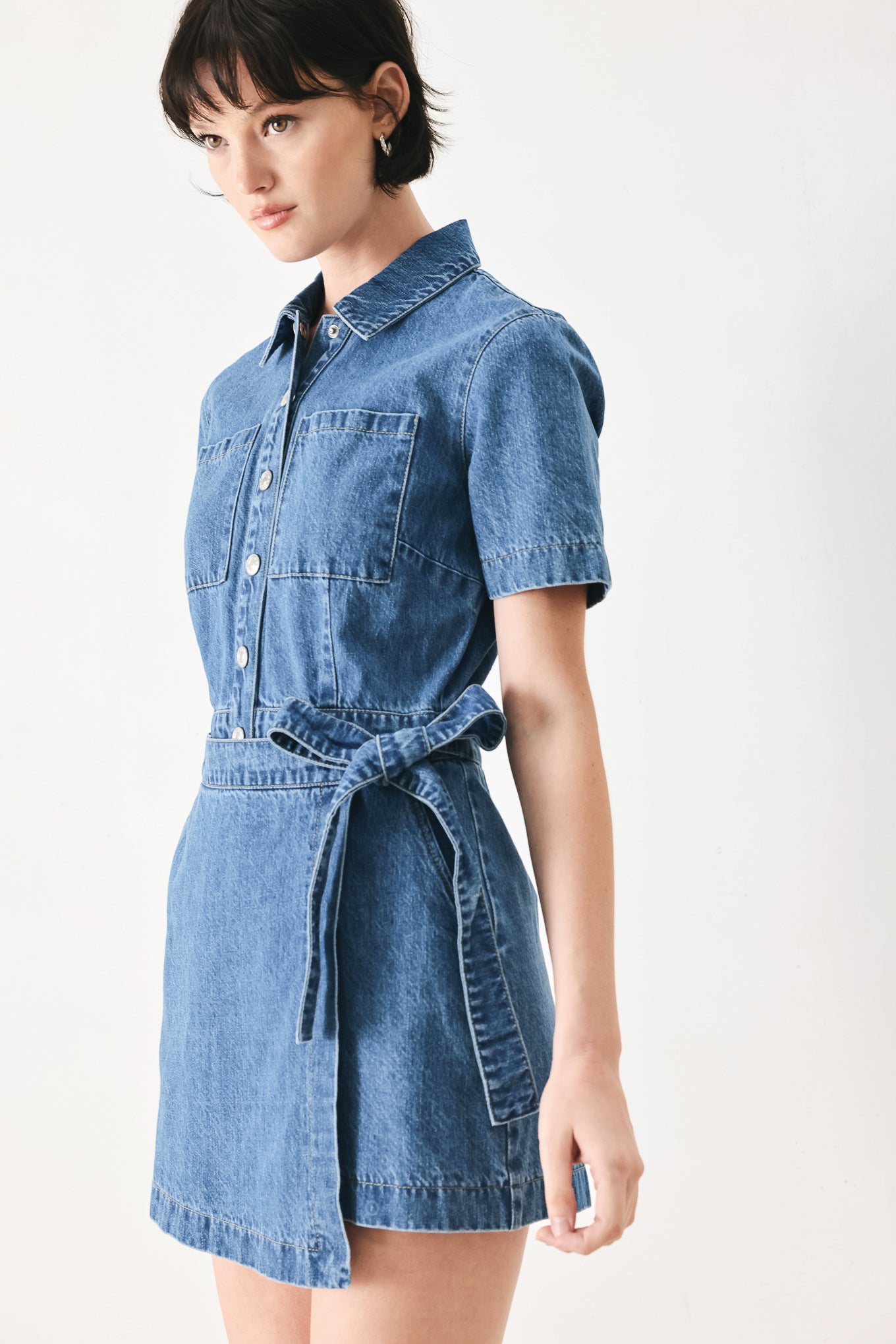 Woman wearing a blue denim skort romper featuring front closure, short sleeve, pockets and side tie | FREEMARKET