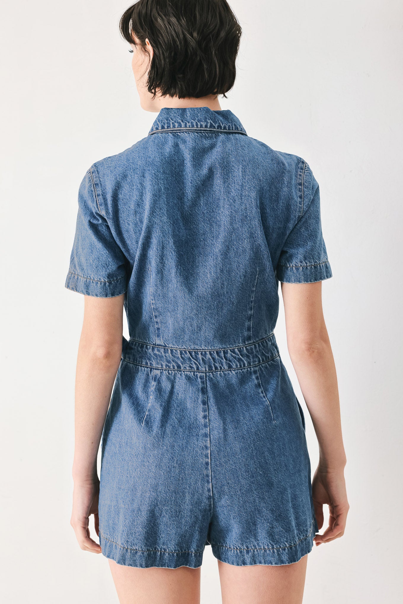 Woman wearing a blue denim skort romper featuring front closure, short sleeve, pockets and side tie | FREEMARKET