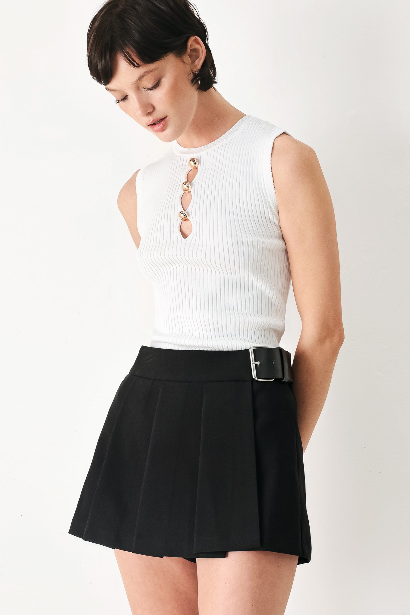 Woman wearing a black pleated skort with a belt buck off side | FREEMARKET
