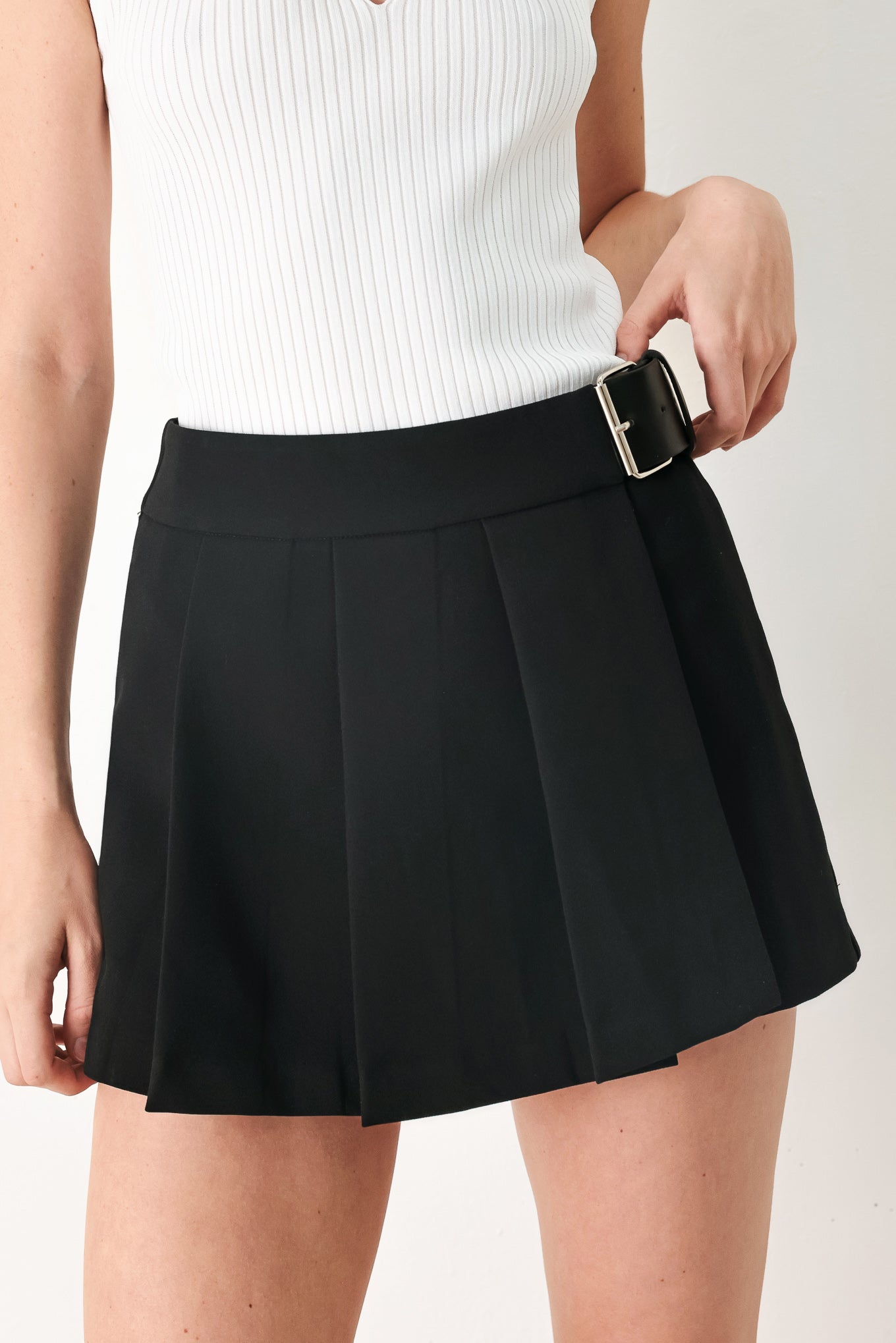 Woman wearing a black pleated skort with a belt buck off side | FREEMARKET