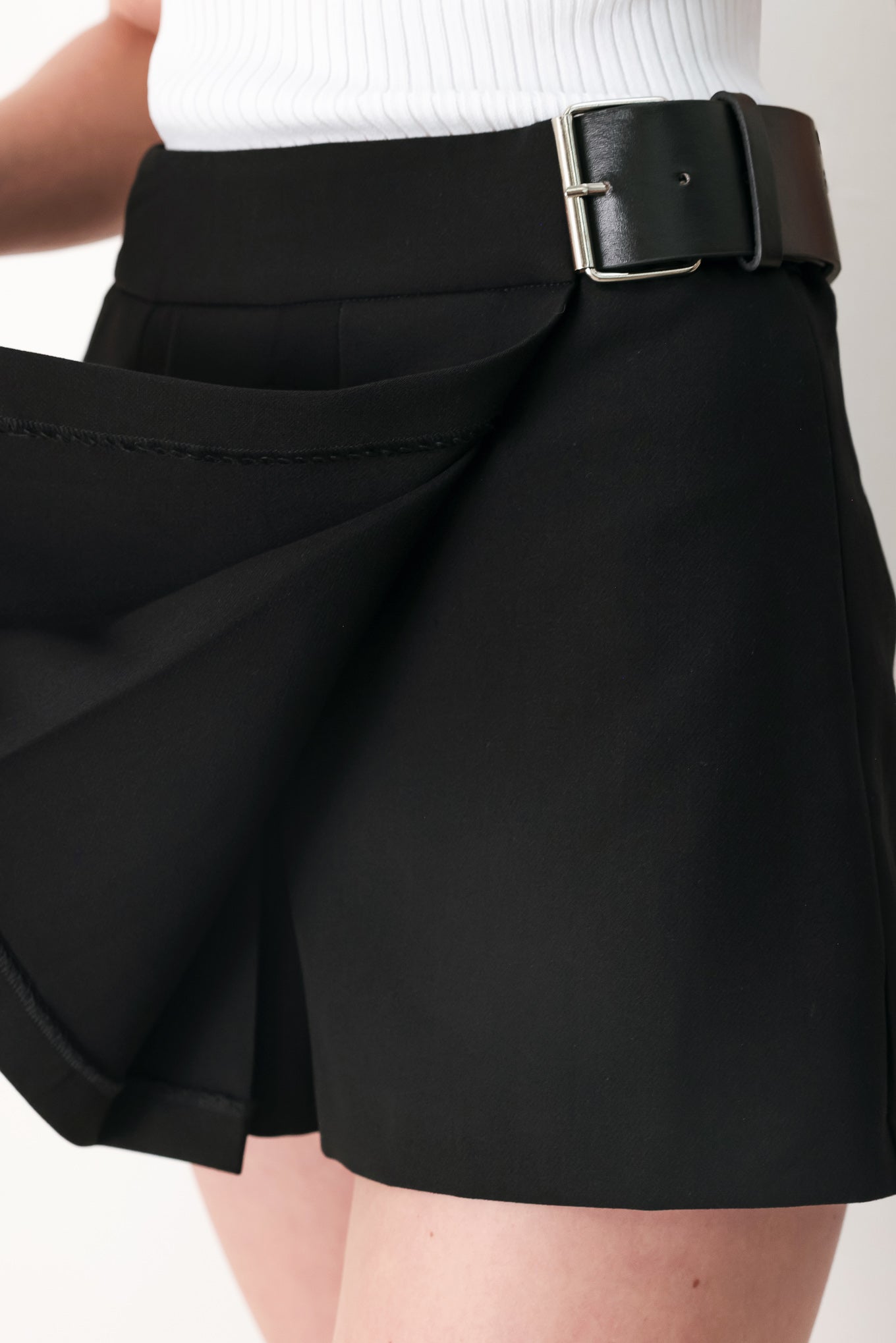 Woman wearing a black pleated skort with a belt buck off side | FREEMARKET